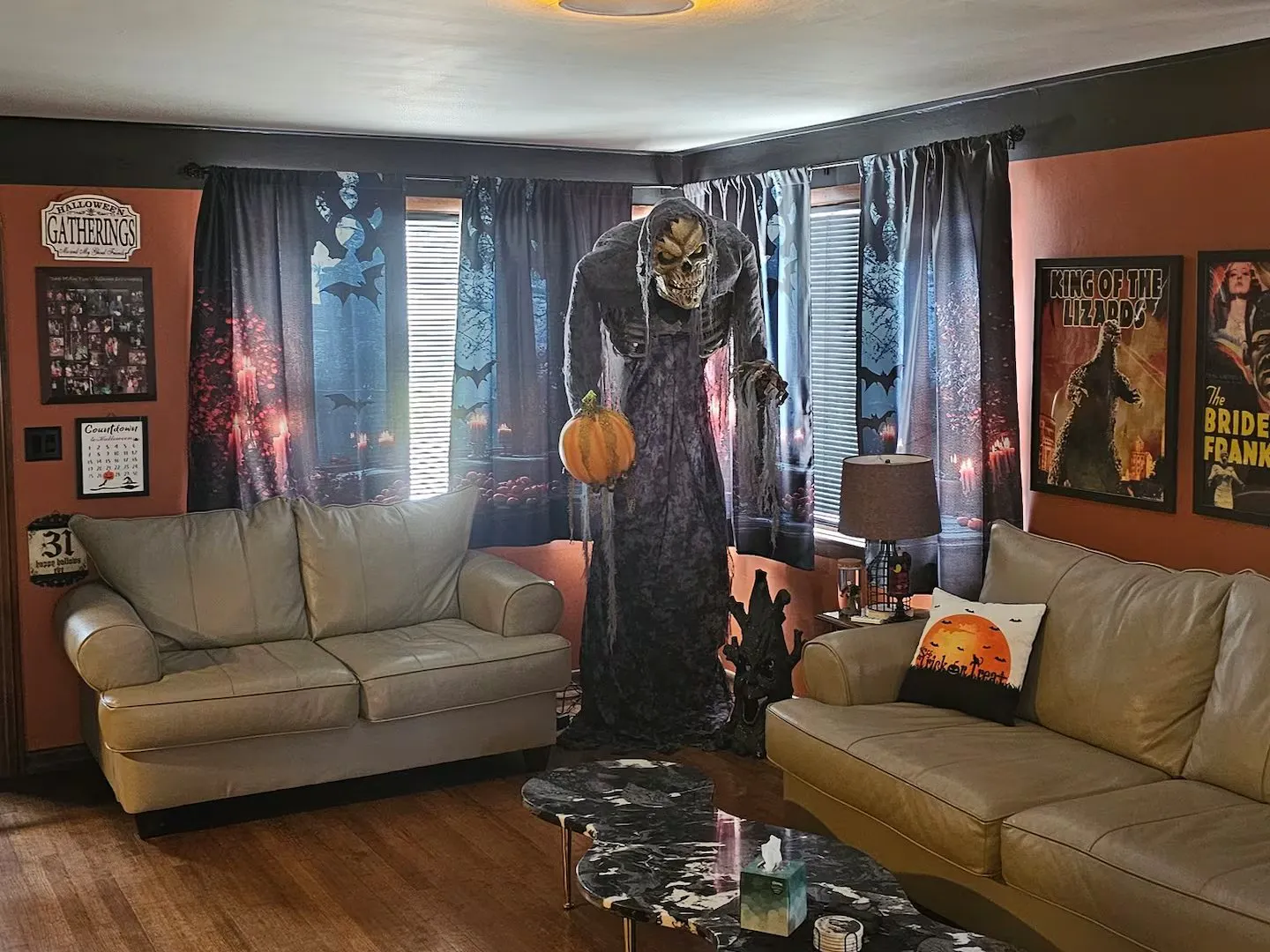 Living room of the Halloween All Year house in Erie, Pennsylvania, with a giant skeleton reaper holding a pumpkin between two sofas and horror movie posters on orange walls