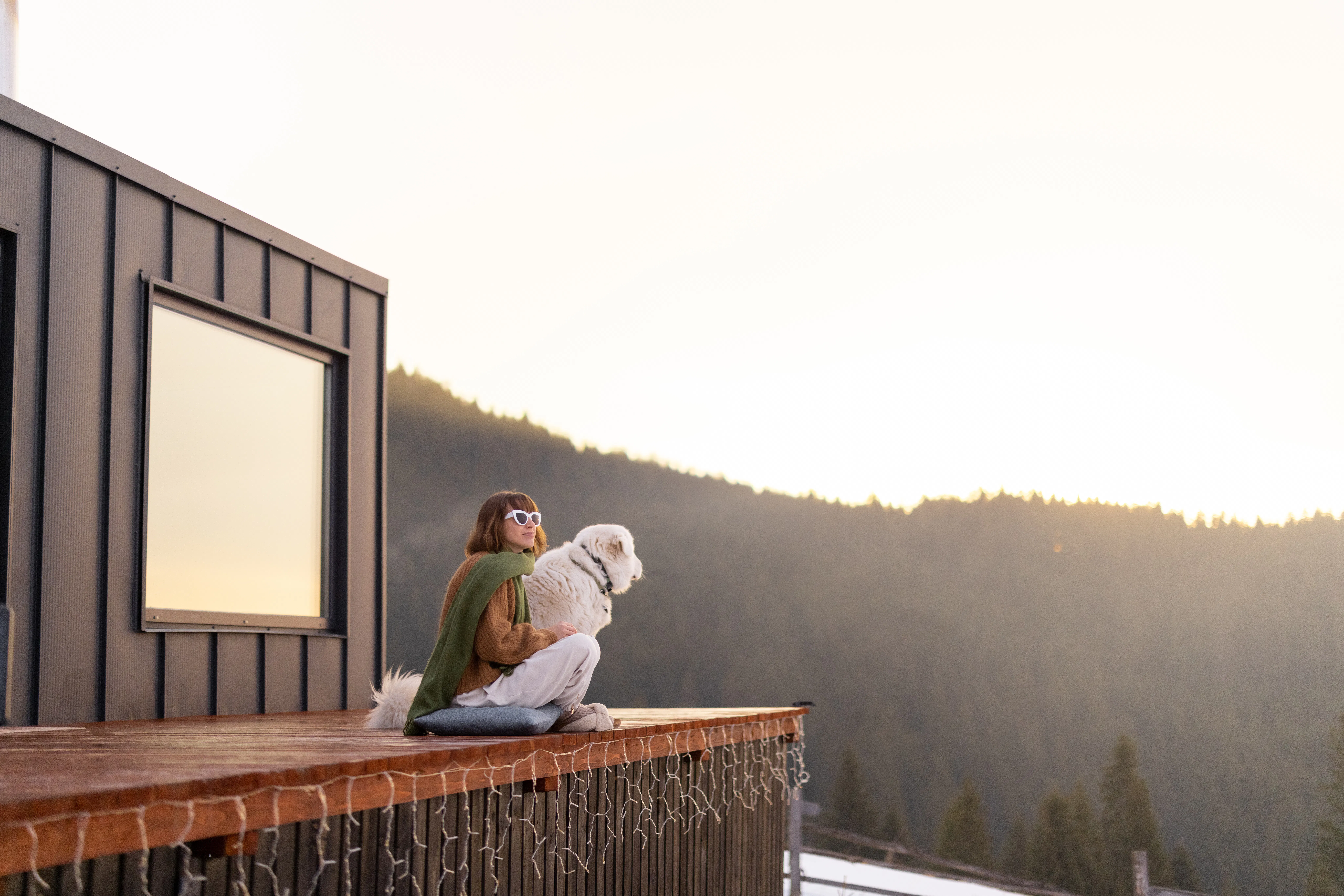 Woman sitting with dog on terrace of tiny house in the mountains