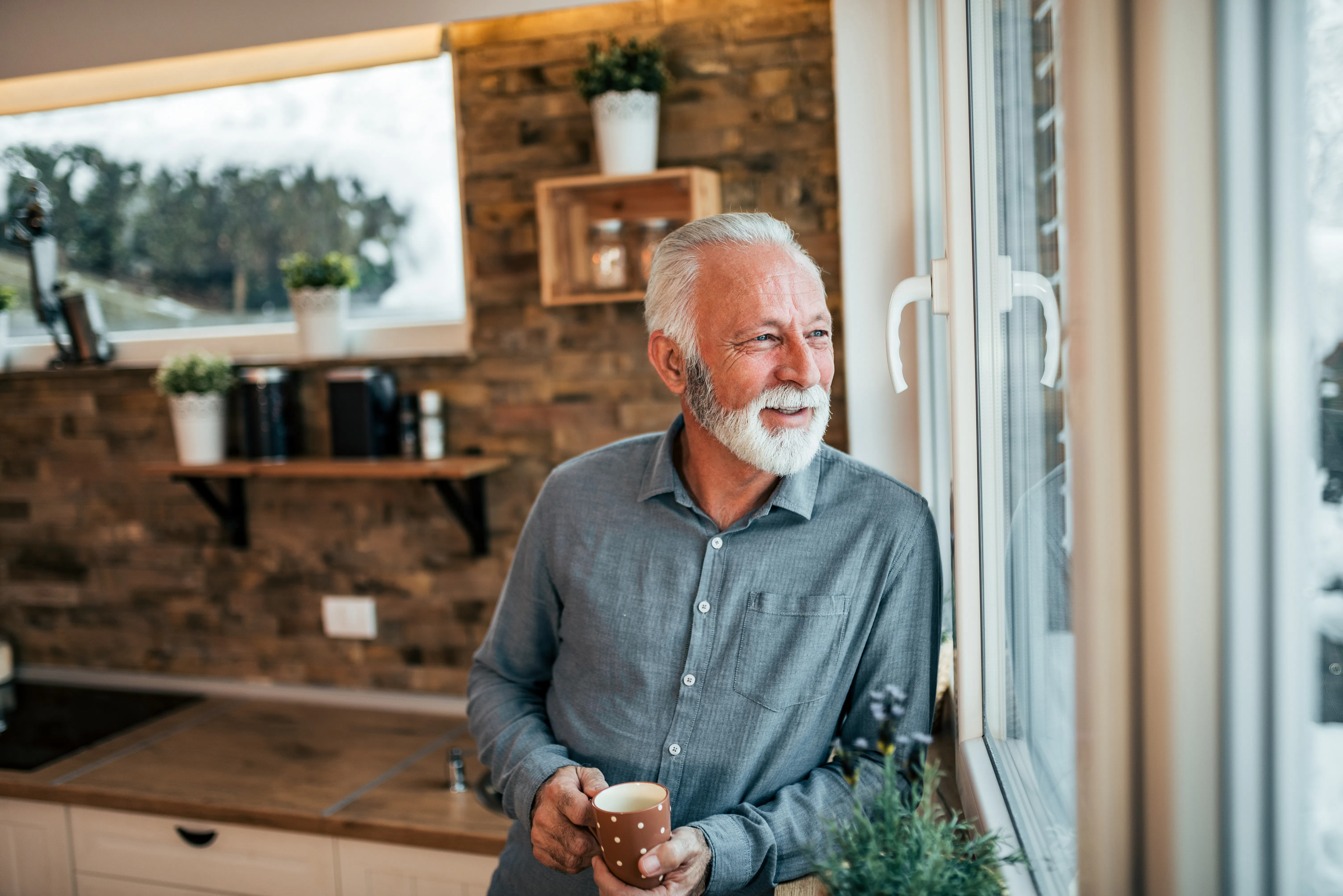 Senior man drinking coffee in the kitchen, looking at window on winter day