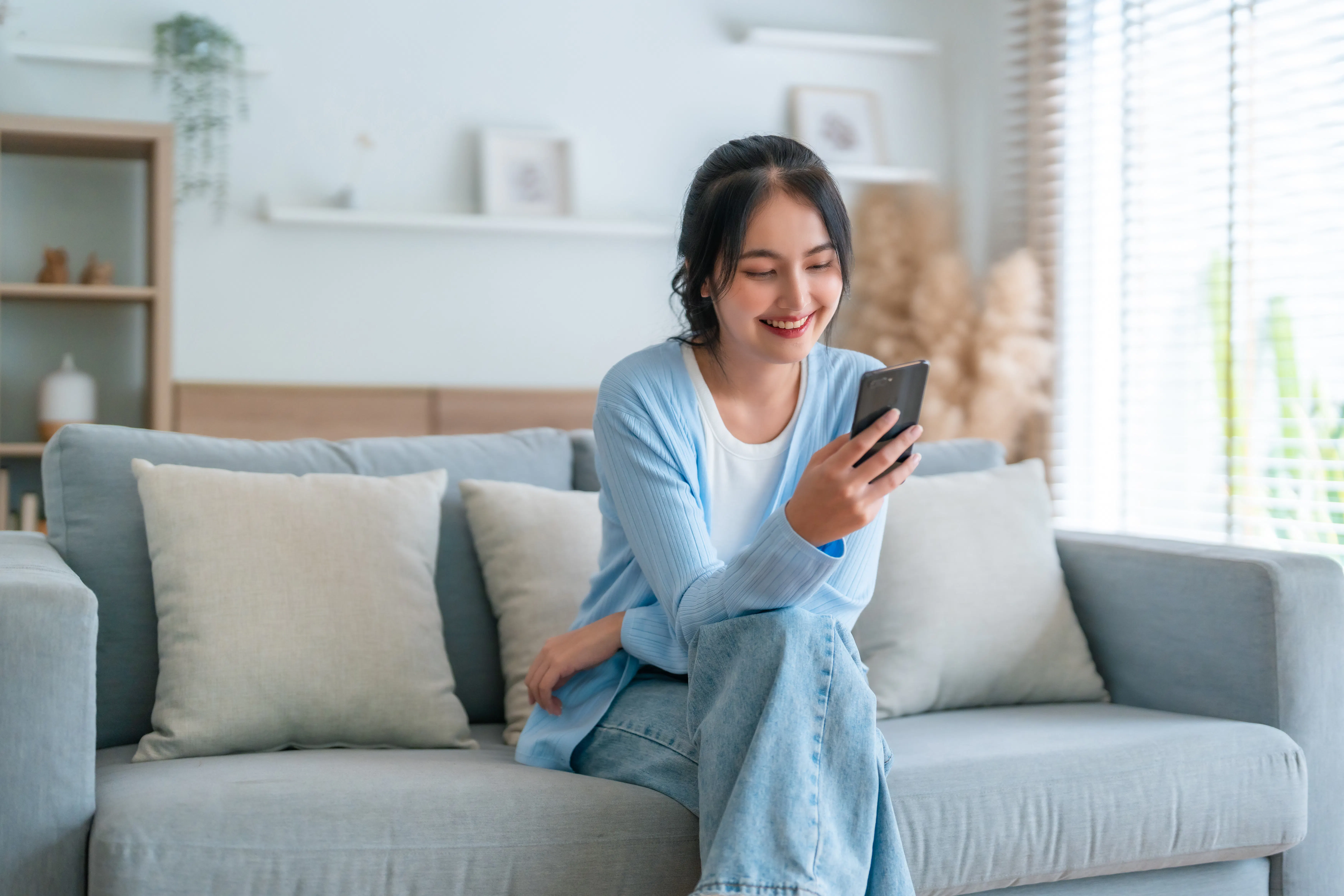 Smiling pretty young Asian woman sitting on cozy couch