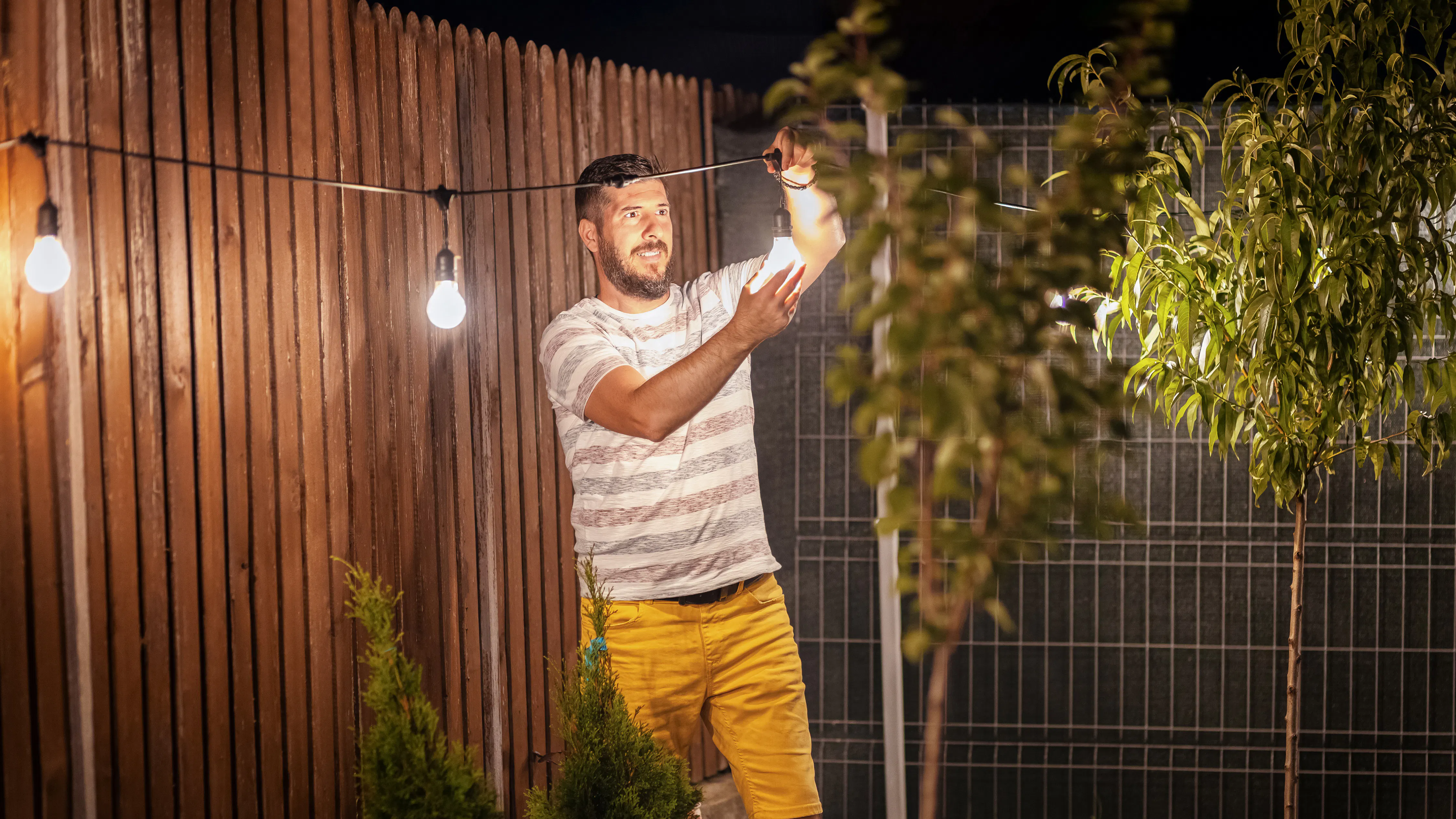 Man hanging string lights in backyard