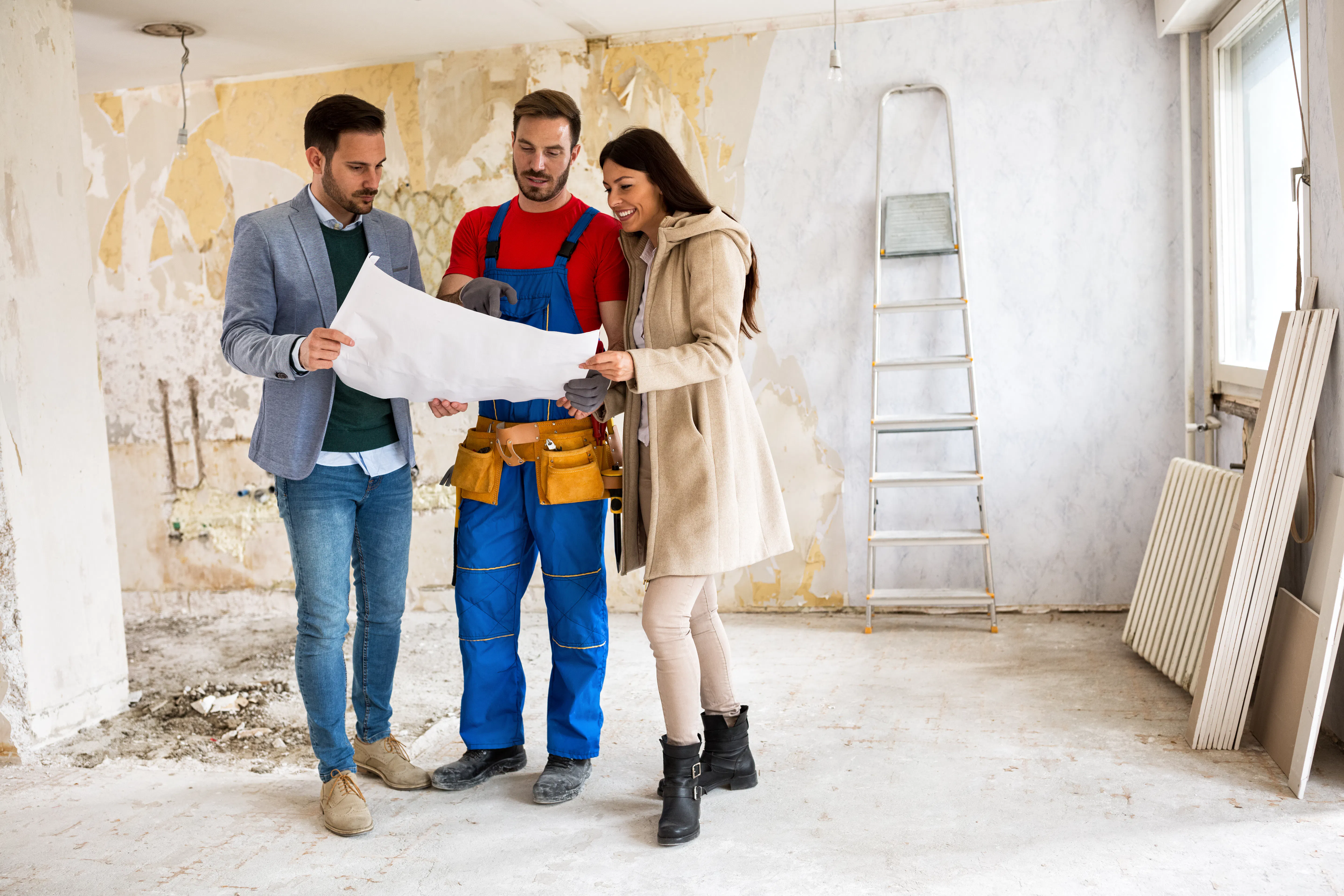 Beautiful young couple looking blueprints of their home with handyman