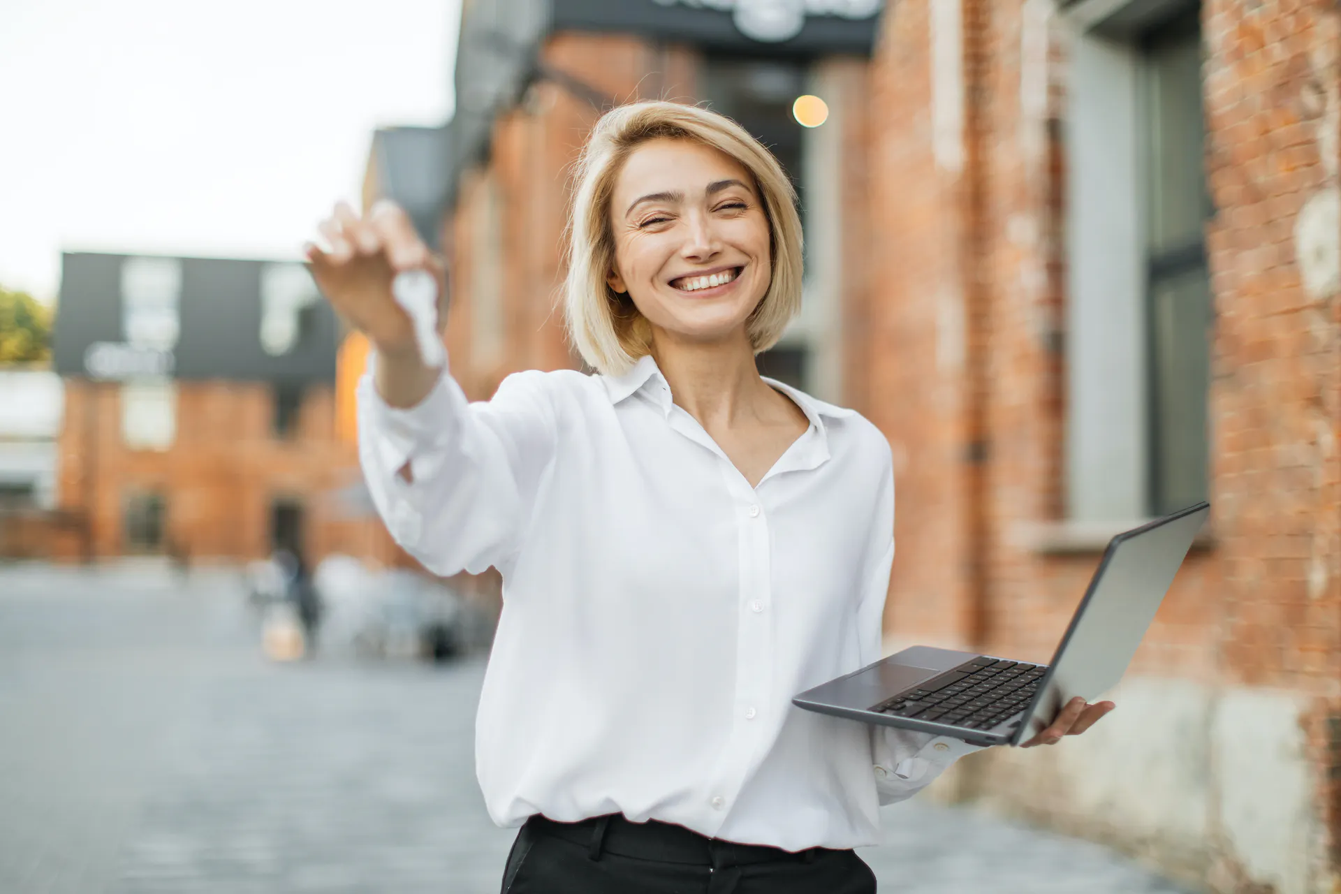 Young Property Manager holding a laptop and showing some keys in front of a vacation rental complex.