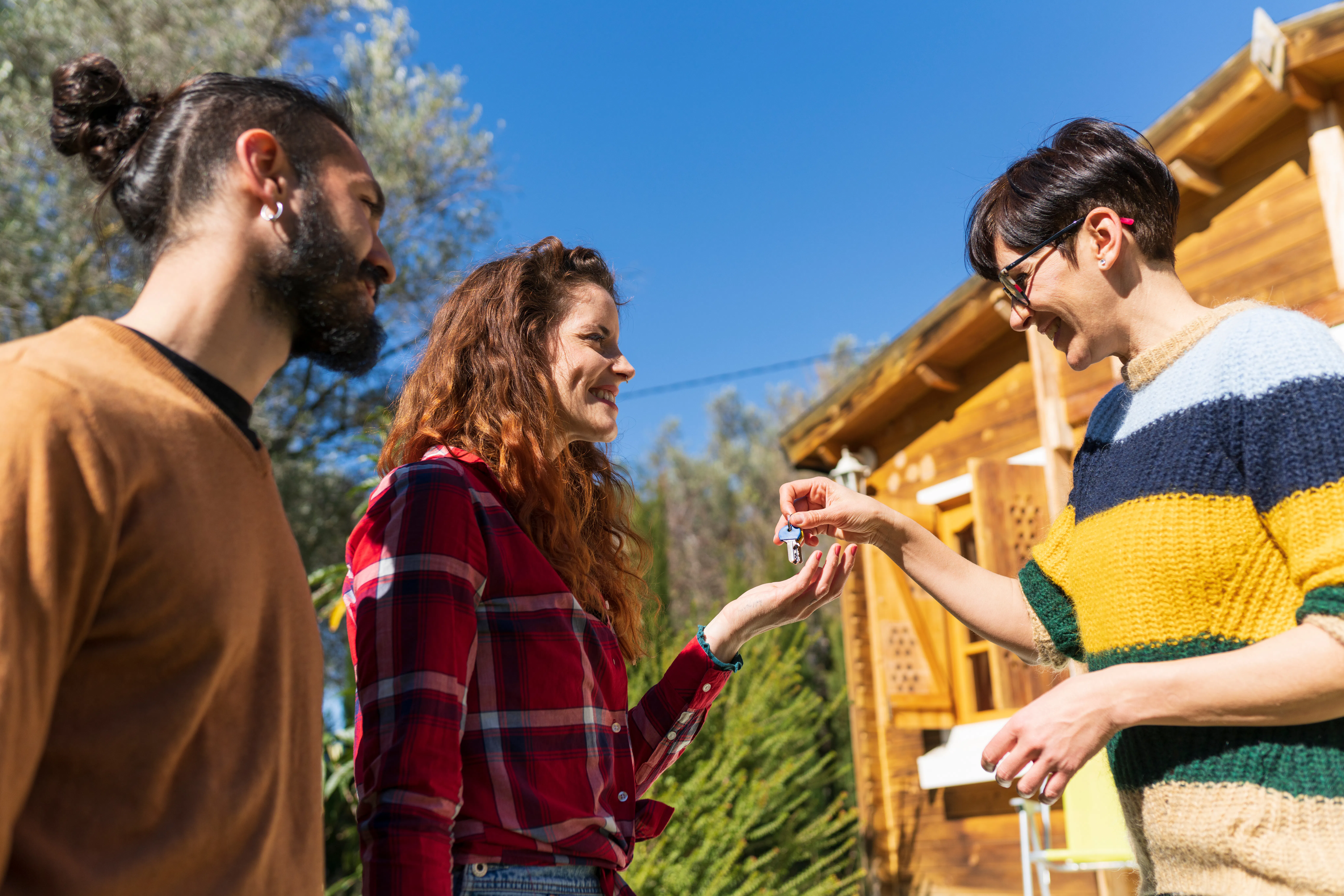 Man handing keys to man and woman outside home