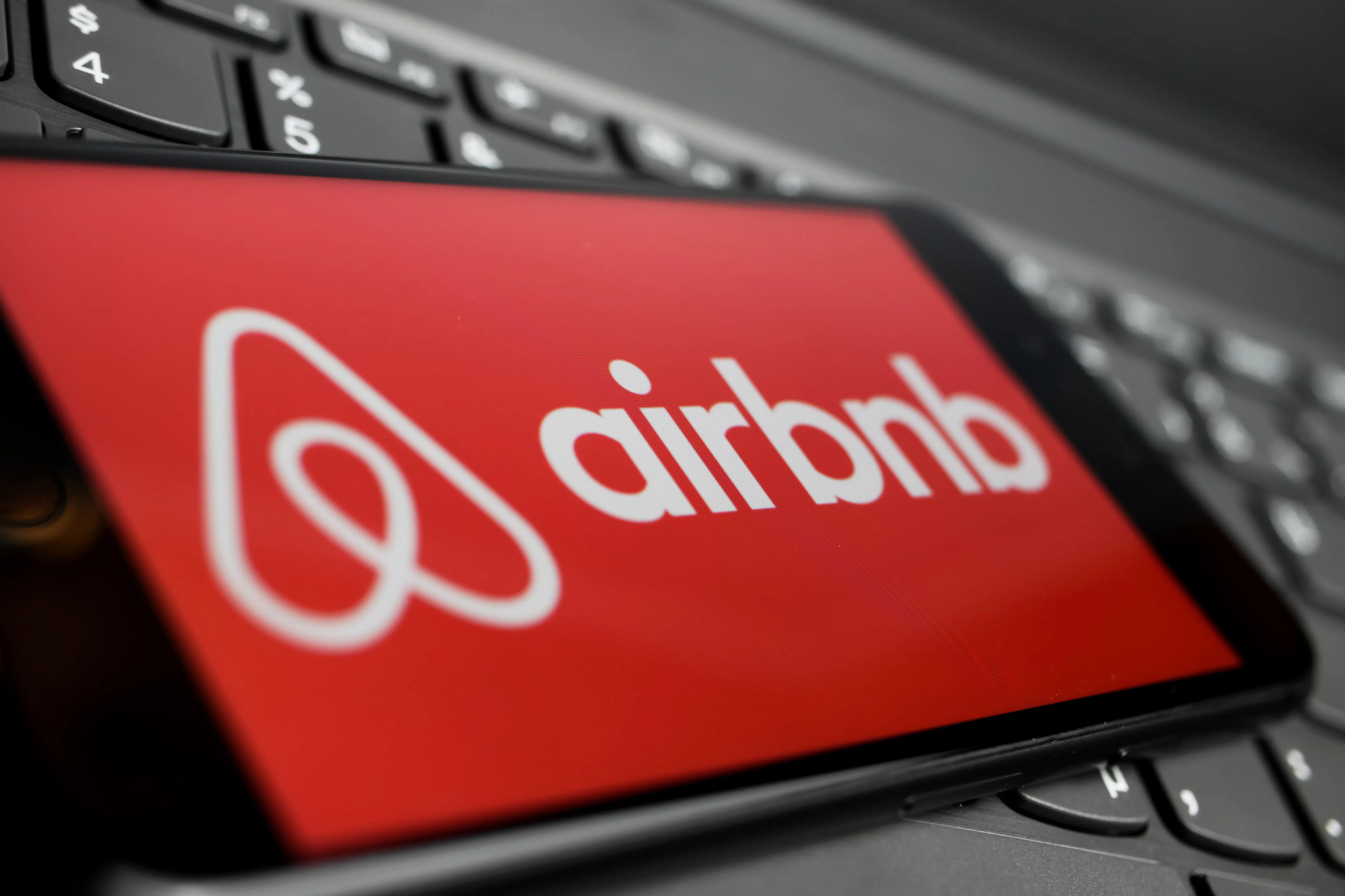 Close up of isolated mobile phone with red airbnb logo lettering on computer keyboard