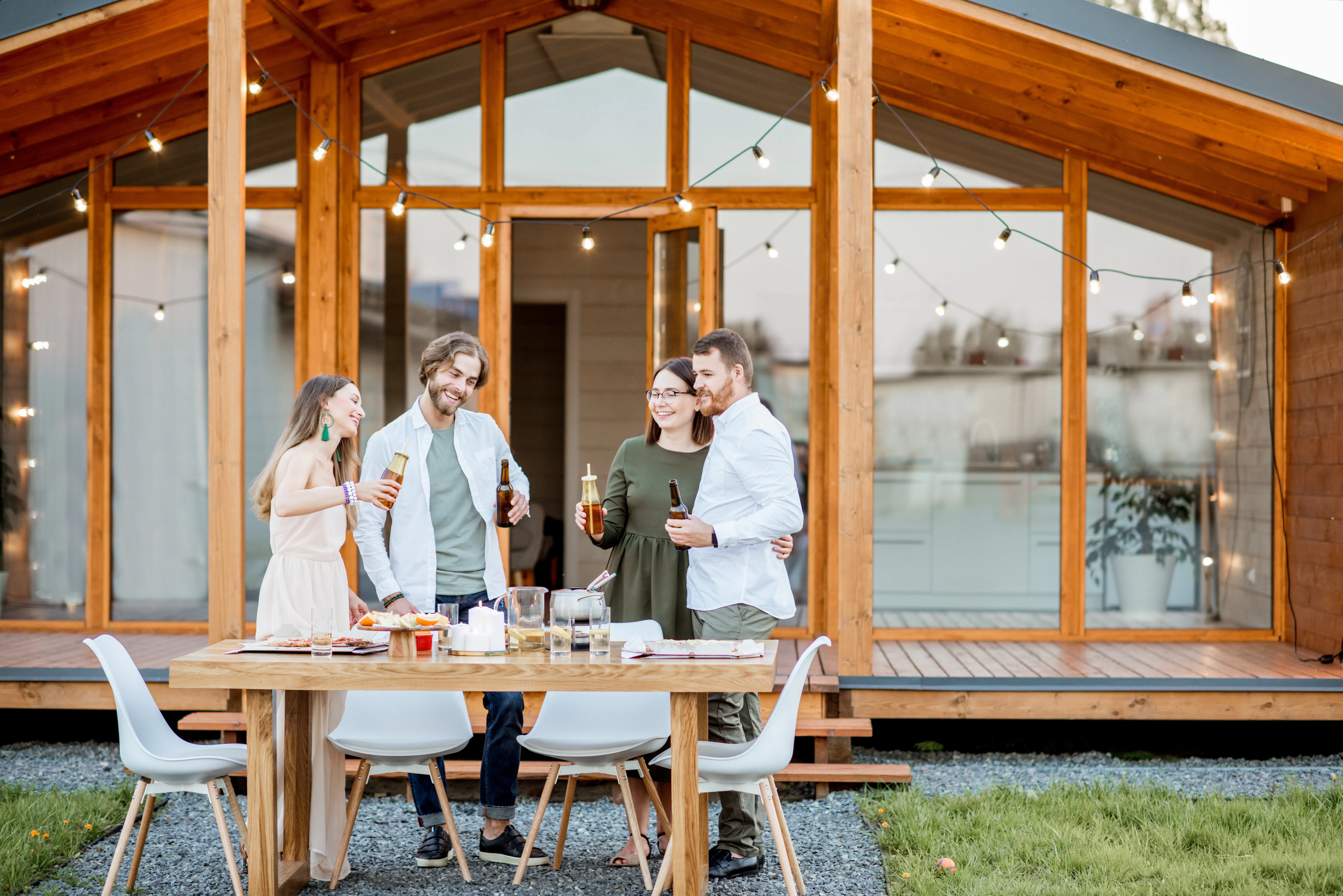 Four friends enjoying evening time together drinking beer on the backyard of the modern country house