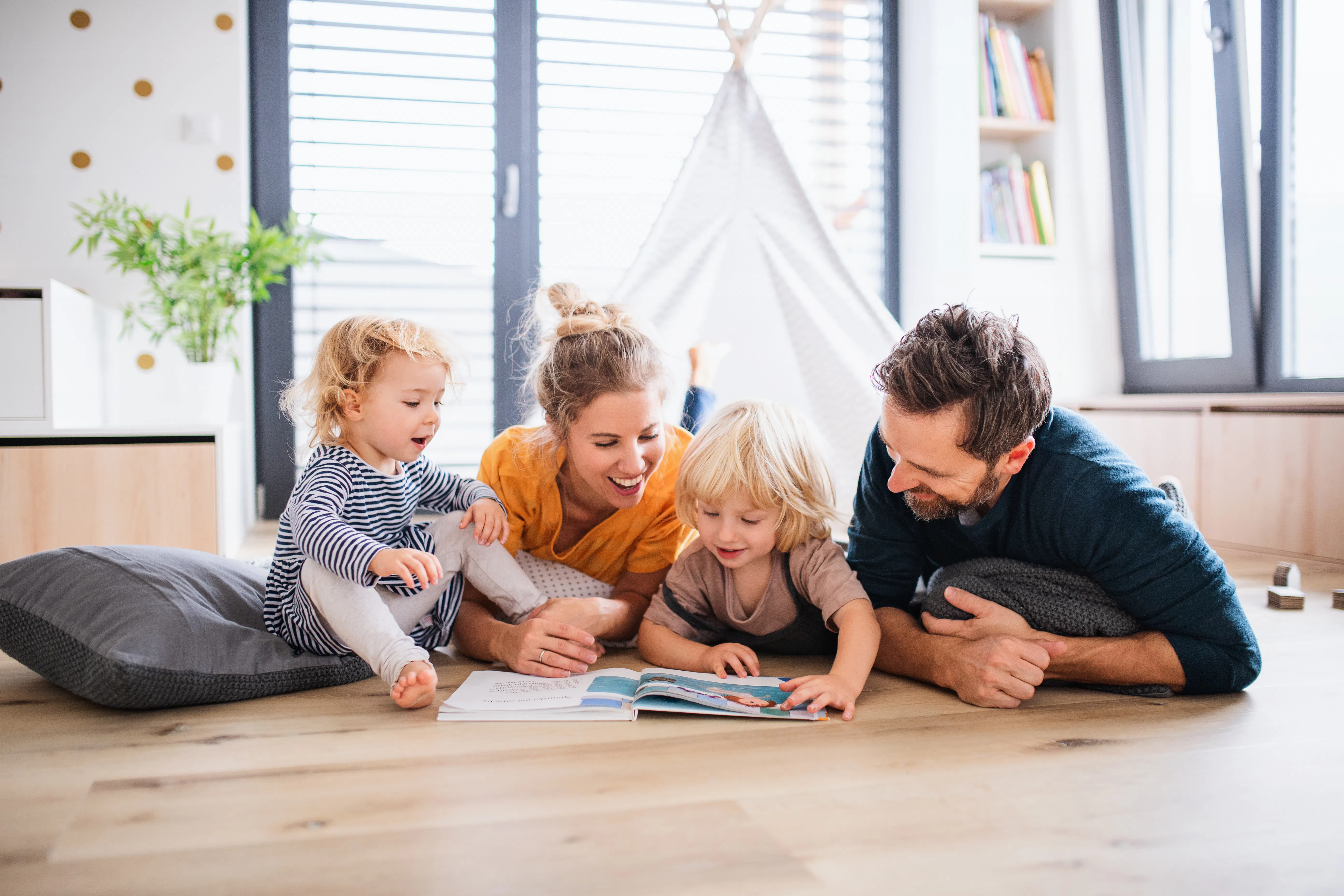 Young family with two small children indoors in bedroom reading a book