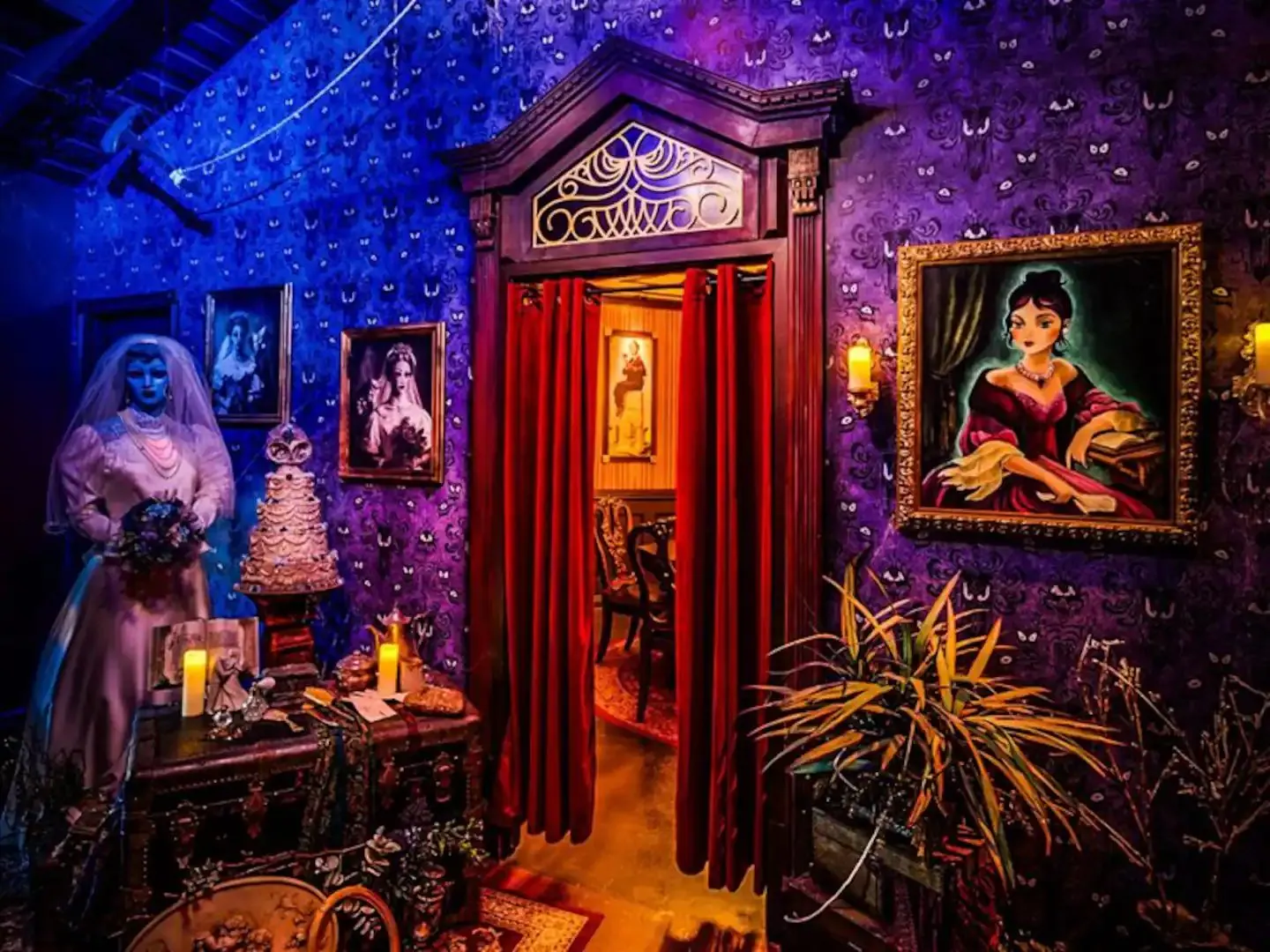 Haunted Mansion-inspired room in Fullerton, California, with purple patterned wallpaper, a ghostly bride figure, gothic portraits and a red-curtained doorway