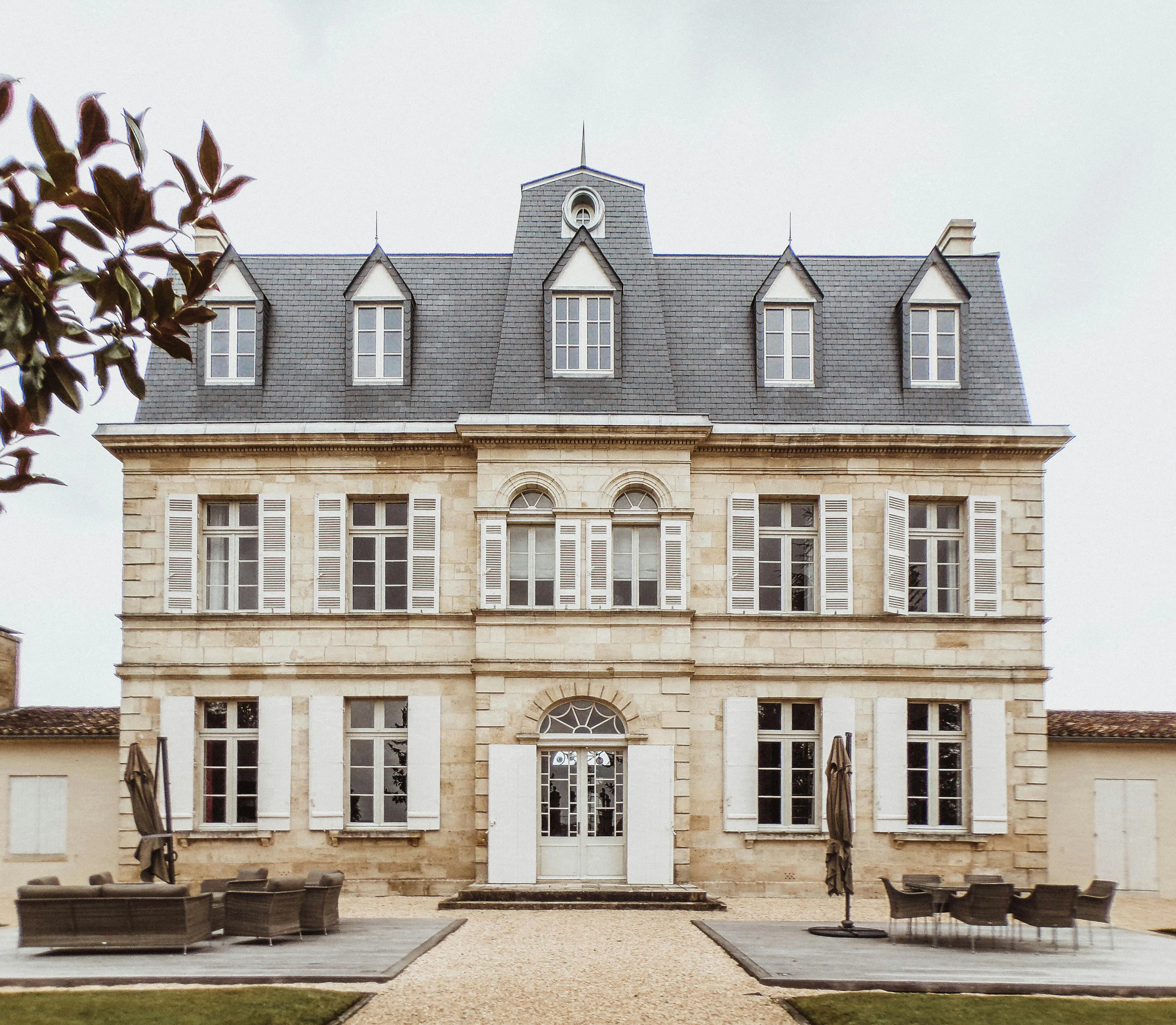 Château en pierre de style français avec toiture en ardoise et espace détente extérieur, sous ciel couvert.