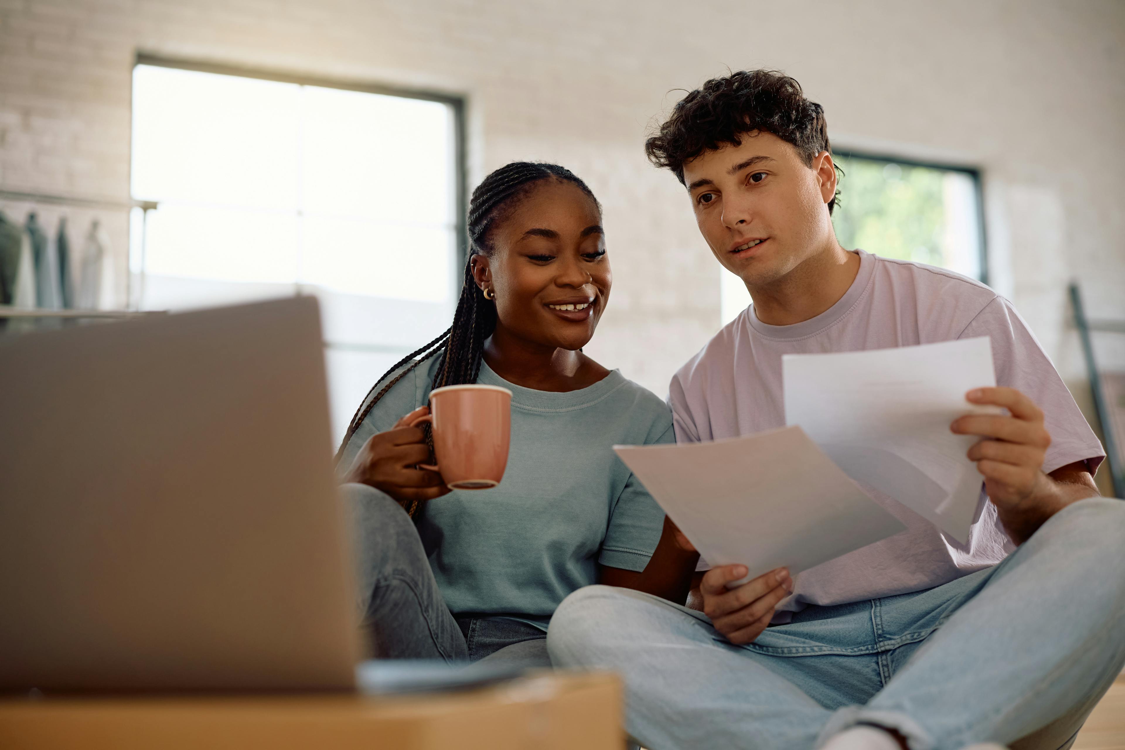 Couple drinking coffee and looking at papers in front of laptop