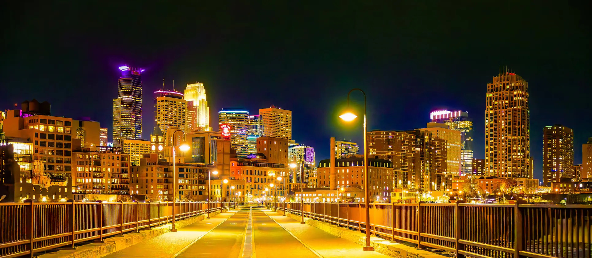 Minneapolis, the downtown skyline lit up at night seen from a pedestrian bridge