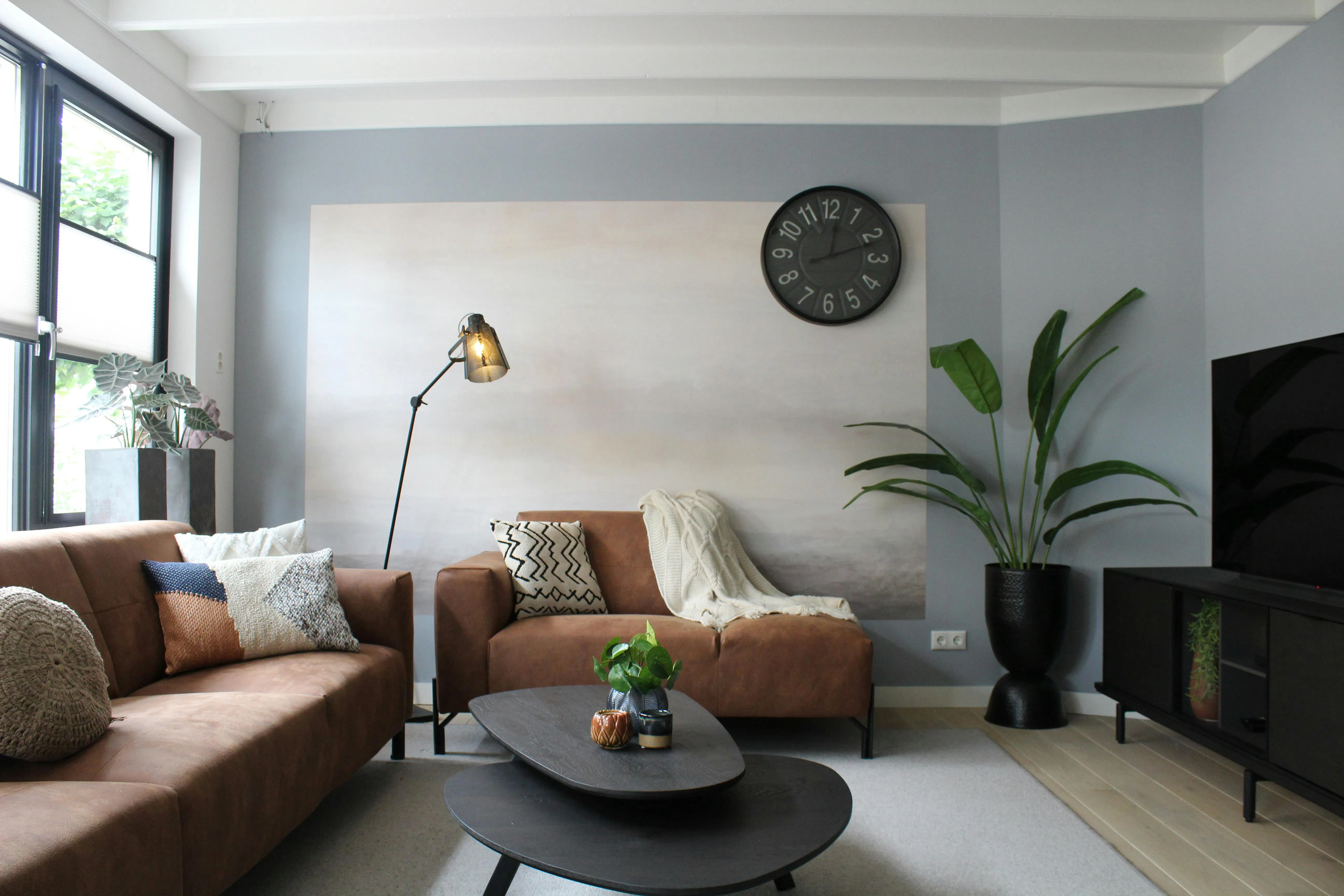 Modern living room with brown couches, a black clock, and a large plant.