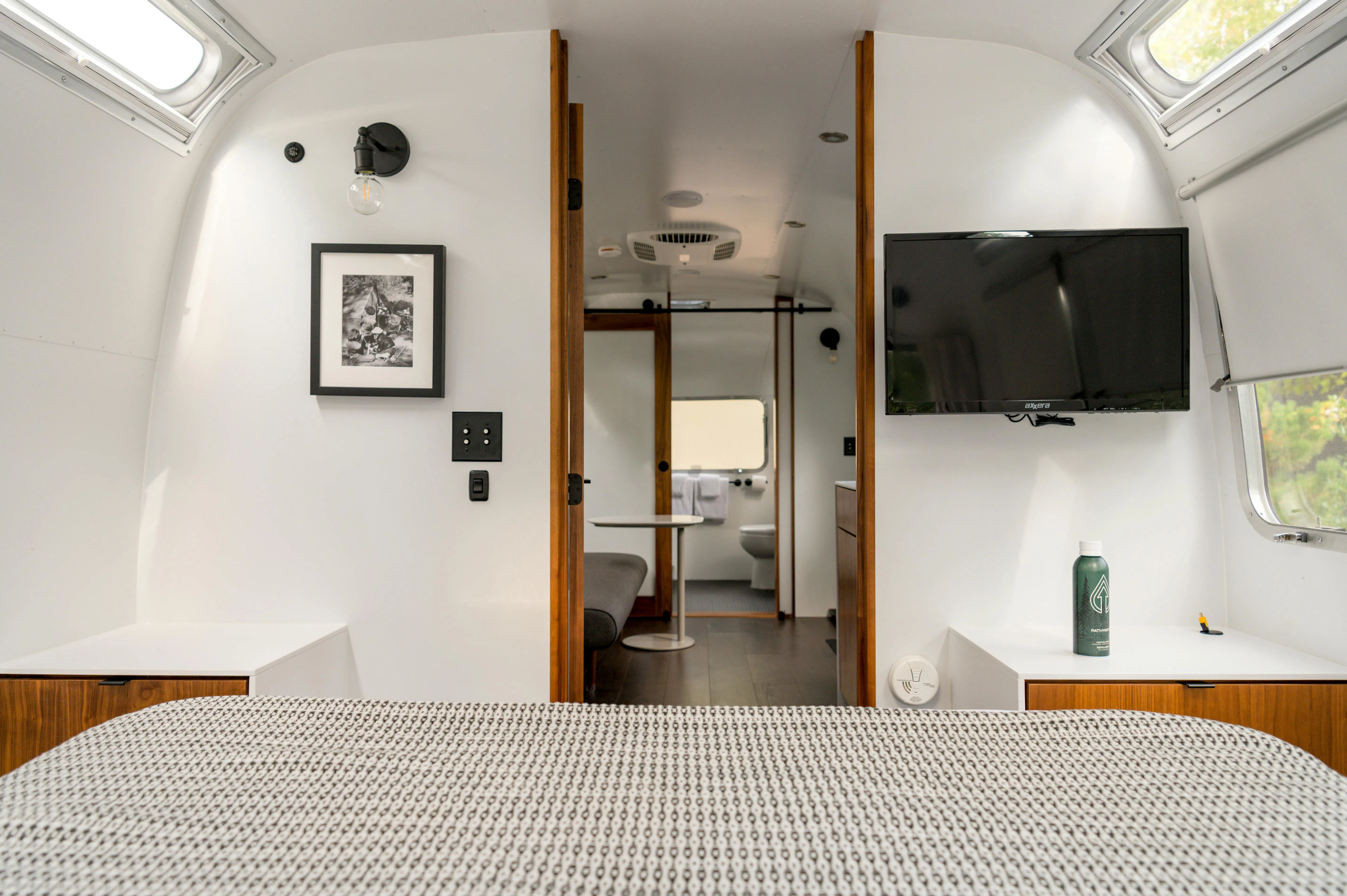 Interior view of an Airstream with a bed, TV, and open bathroom door.