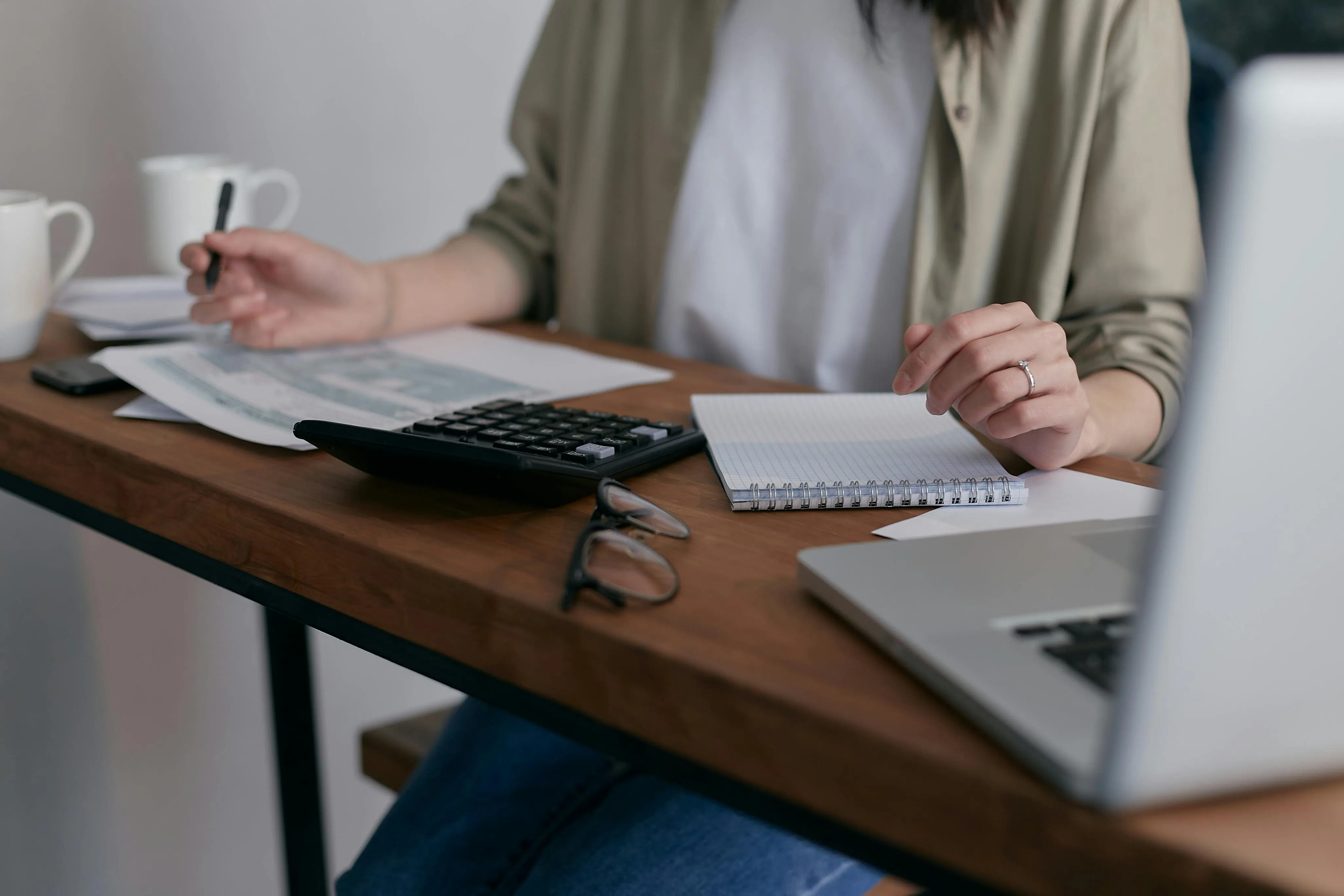 Person reviewing documents with a calculator, notebook, and laptop.