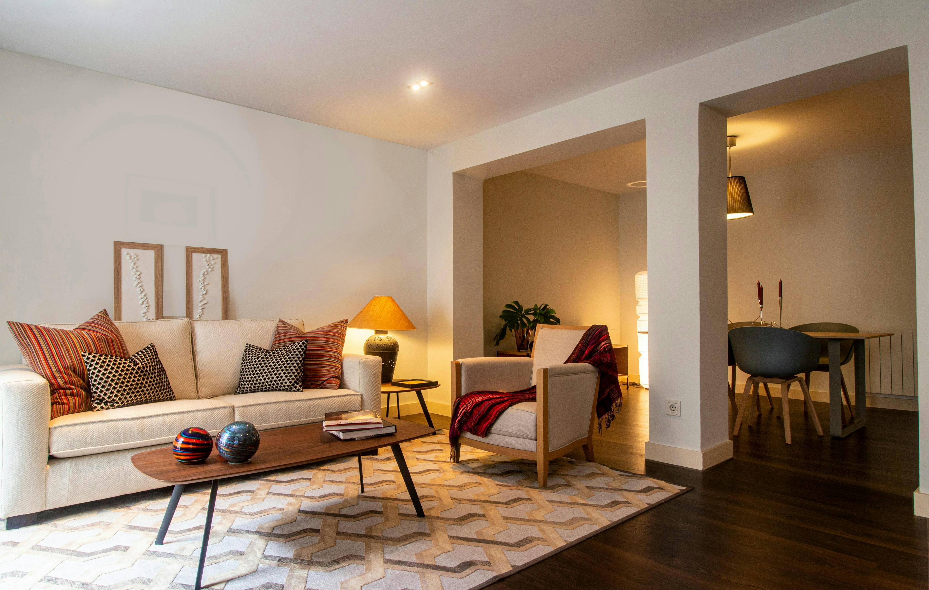 Warm living room with neutral couch, patterned rug, and a dining area beyond.
