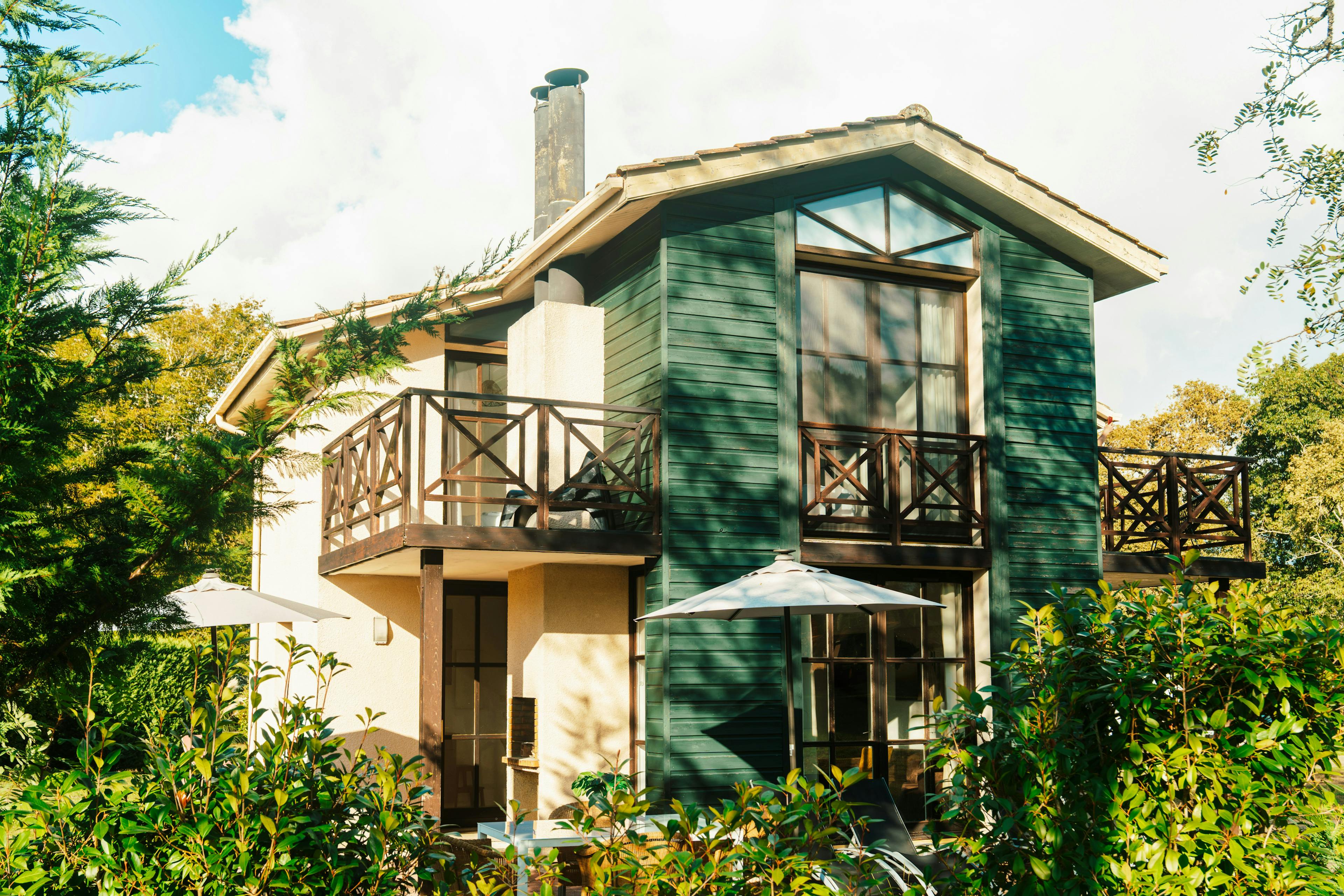 Green and beige house exterior with balconies and white patio umbrellas.