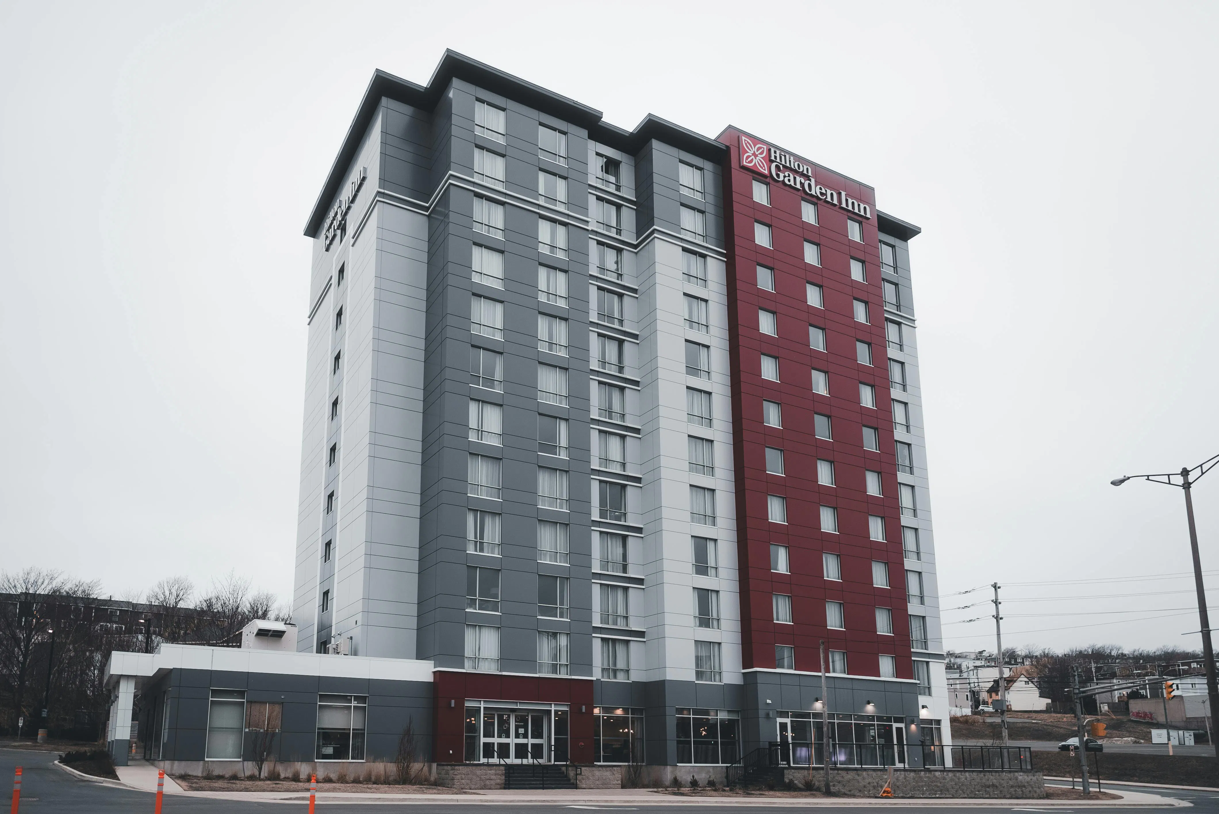 A high-rise Hilton Garden Inn hotel building with gray, white, and red exterior panels under an overcast sky.