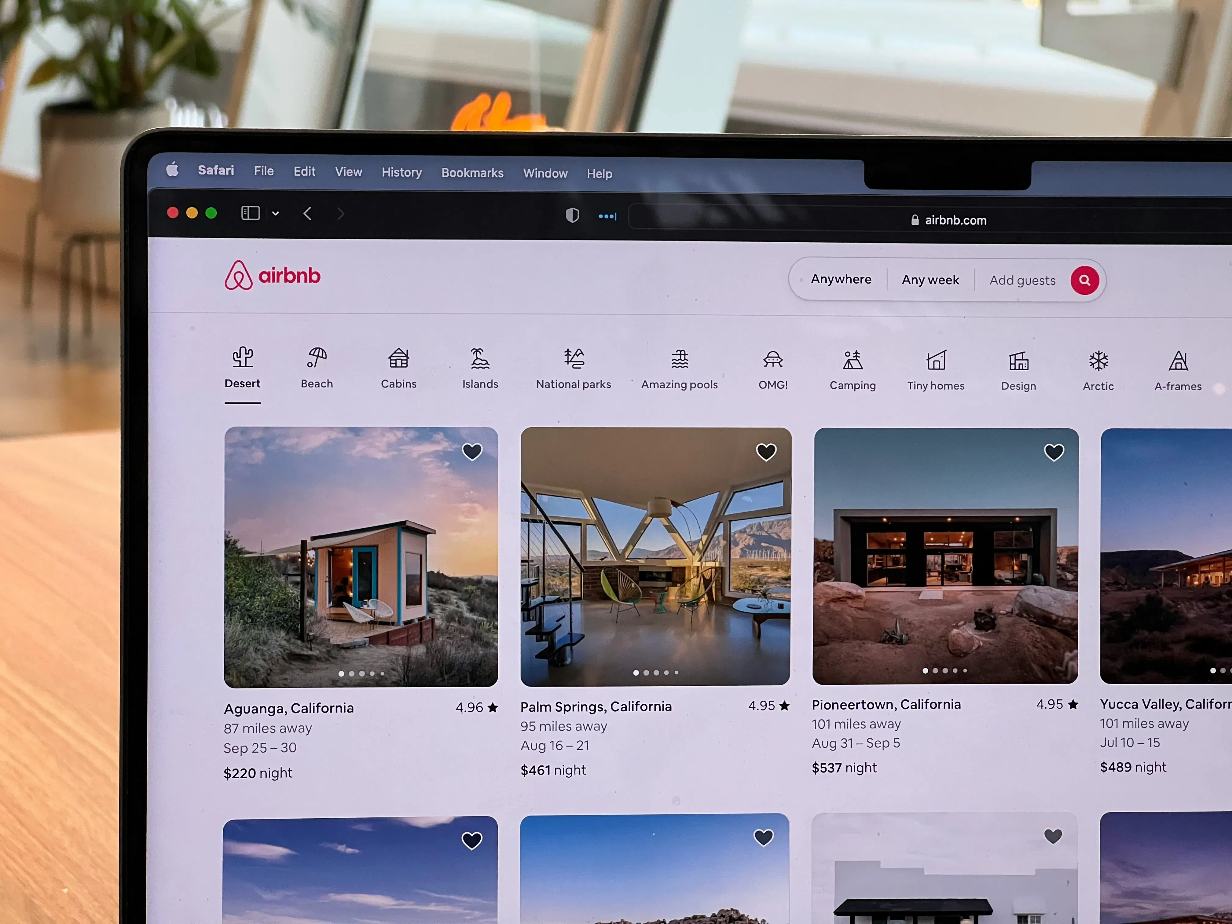 The Airbnb website open on a laptop screen, showing various desert vacation rental listings in California.