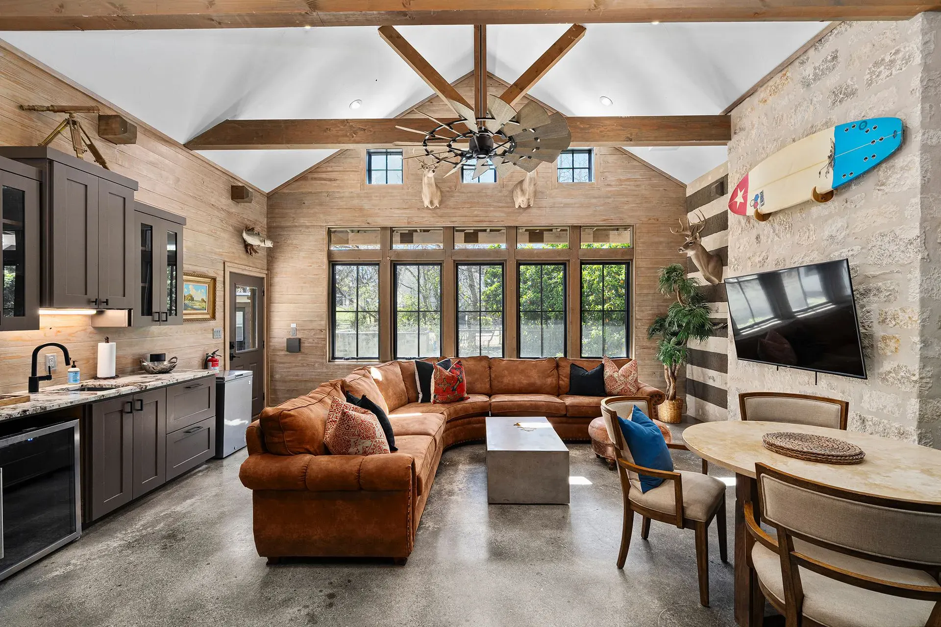Living room in a Bach Bros Properties home with a leather sectional, vaulted wood beam ceiling, stone wall and kitchenette