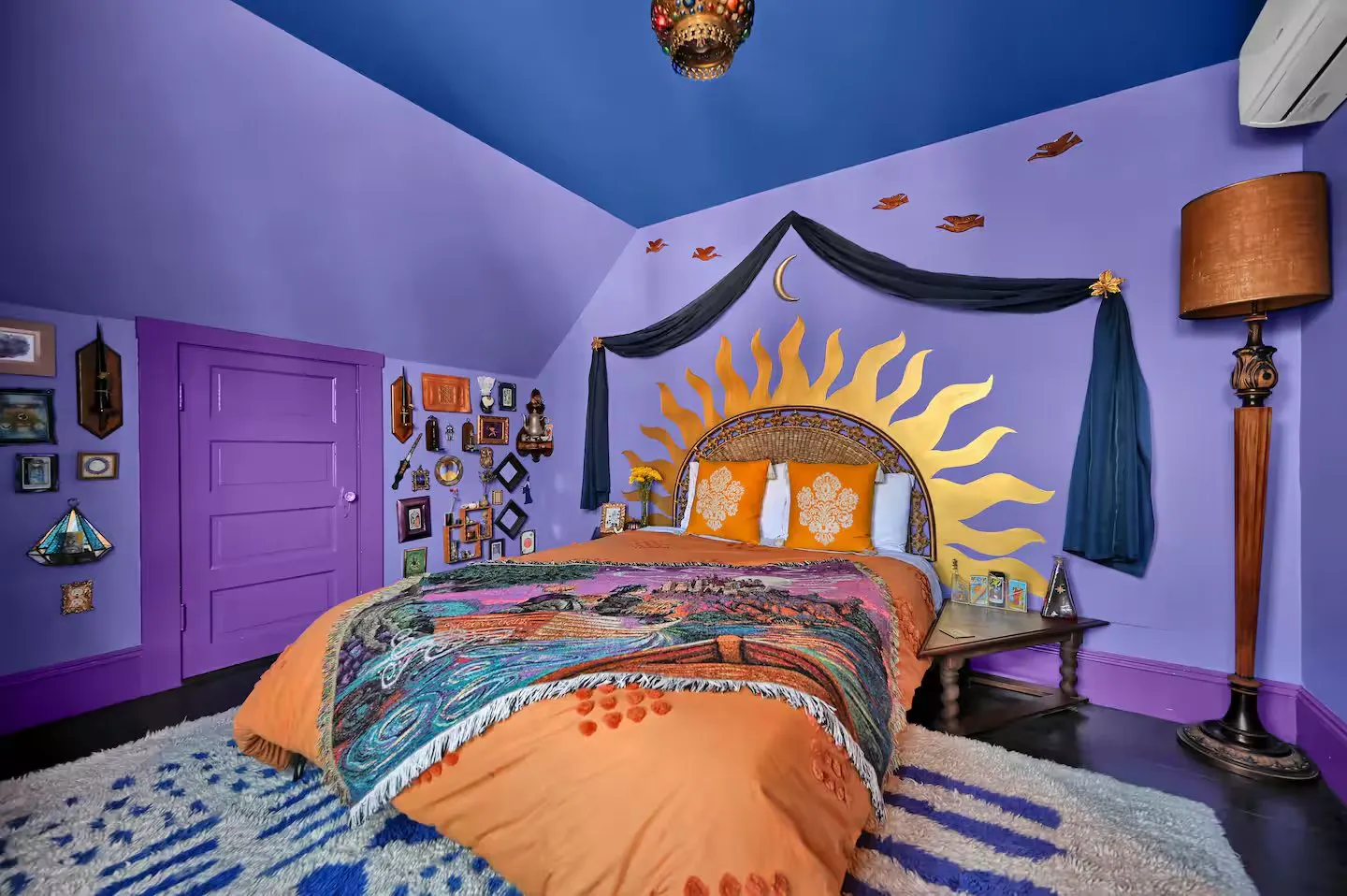 Purple attic bedroom at The Ghoul’s Attic in Salem, Massachusetts, with a golden sun headboard and an orange bedspread