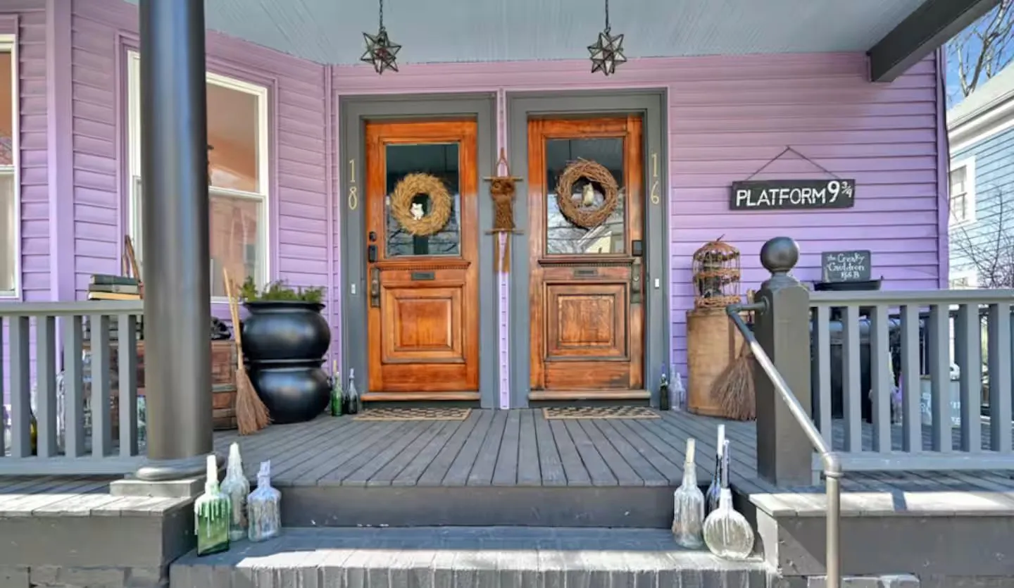 Front porch of The Creaky Cauldron in Salem, Massachusetts, with a black cauldron, a broom, apothecary bottles and a train platform sign beside two wooden doors