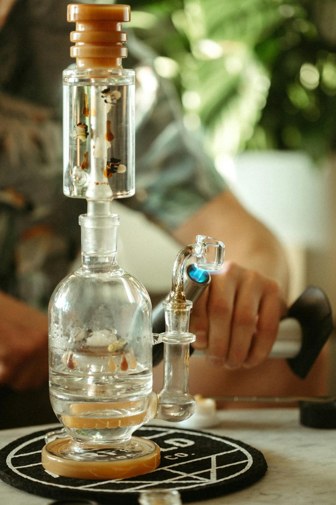 A bong with a person torching the glass tip preparing for a dab 