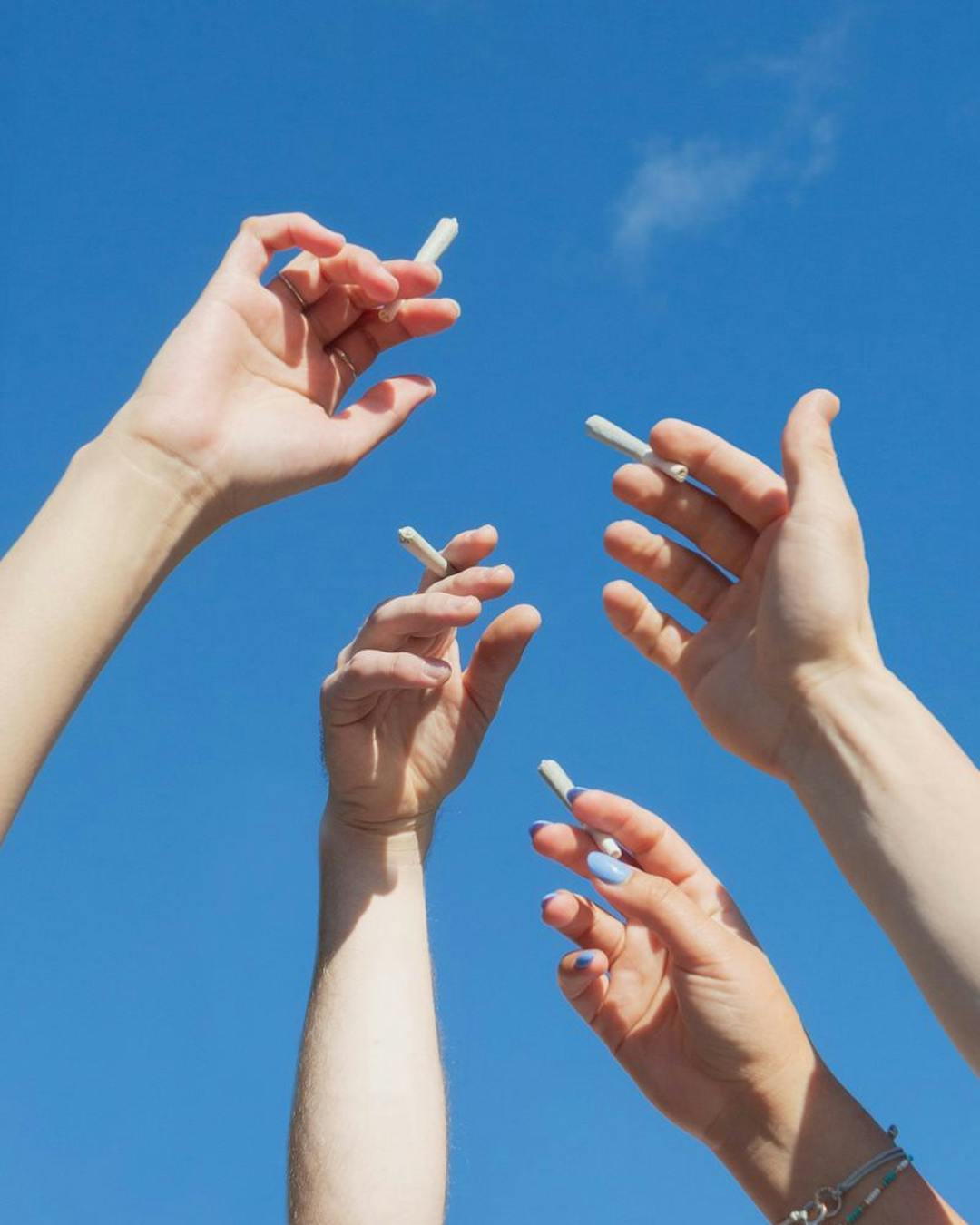 4 hands holding up cannabis joints in air