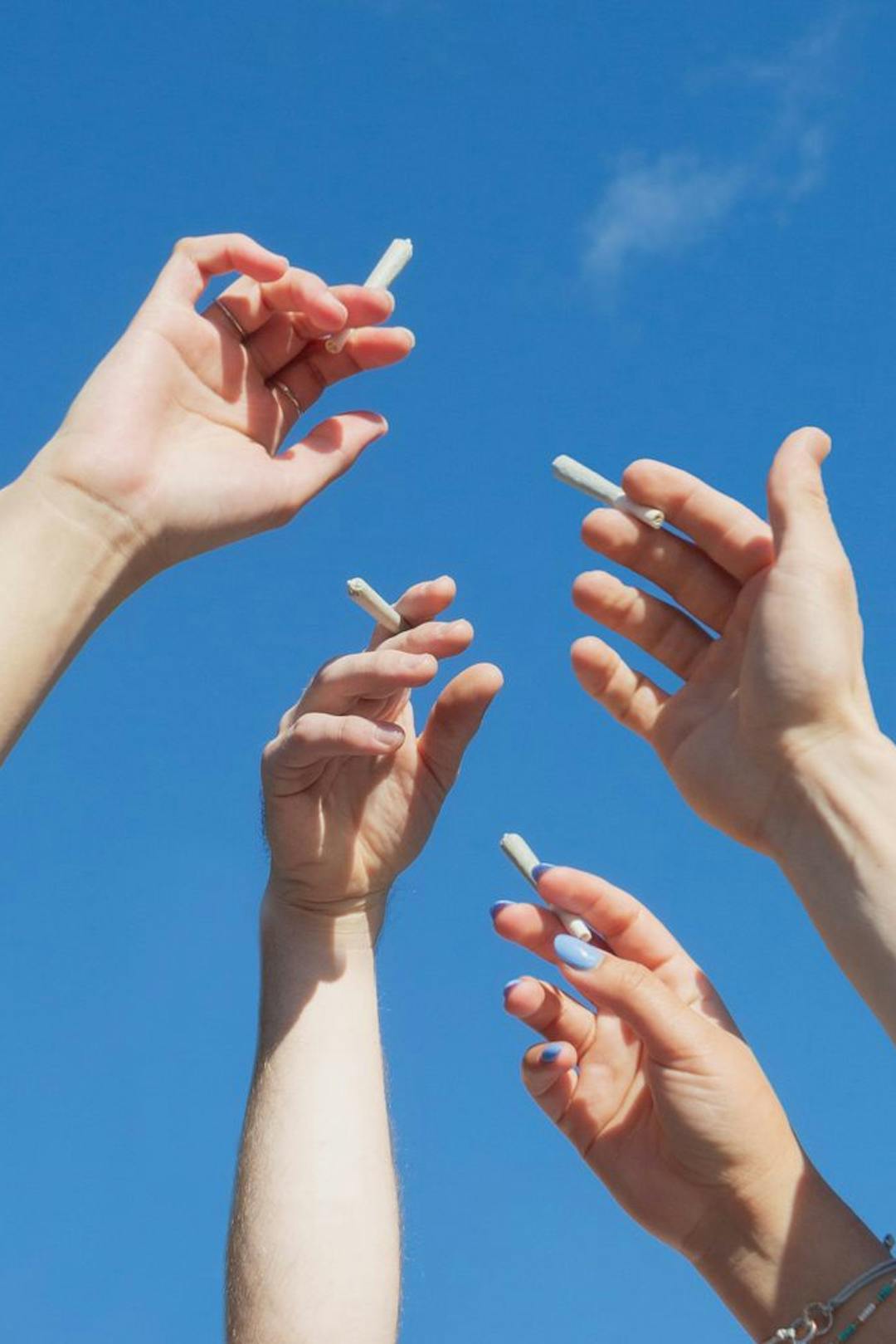 4 hands holding up cannabis joints in air