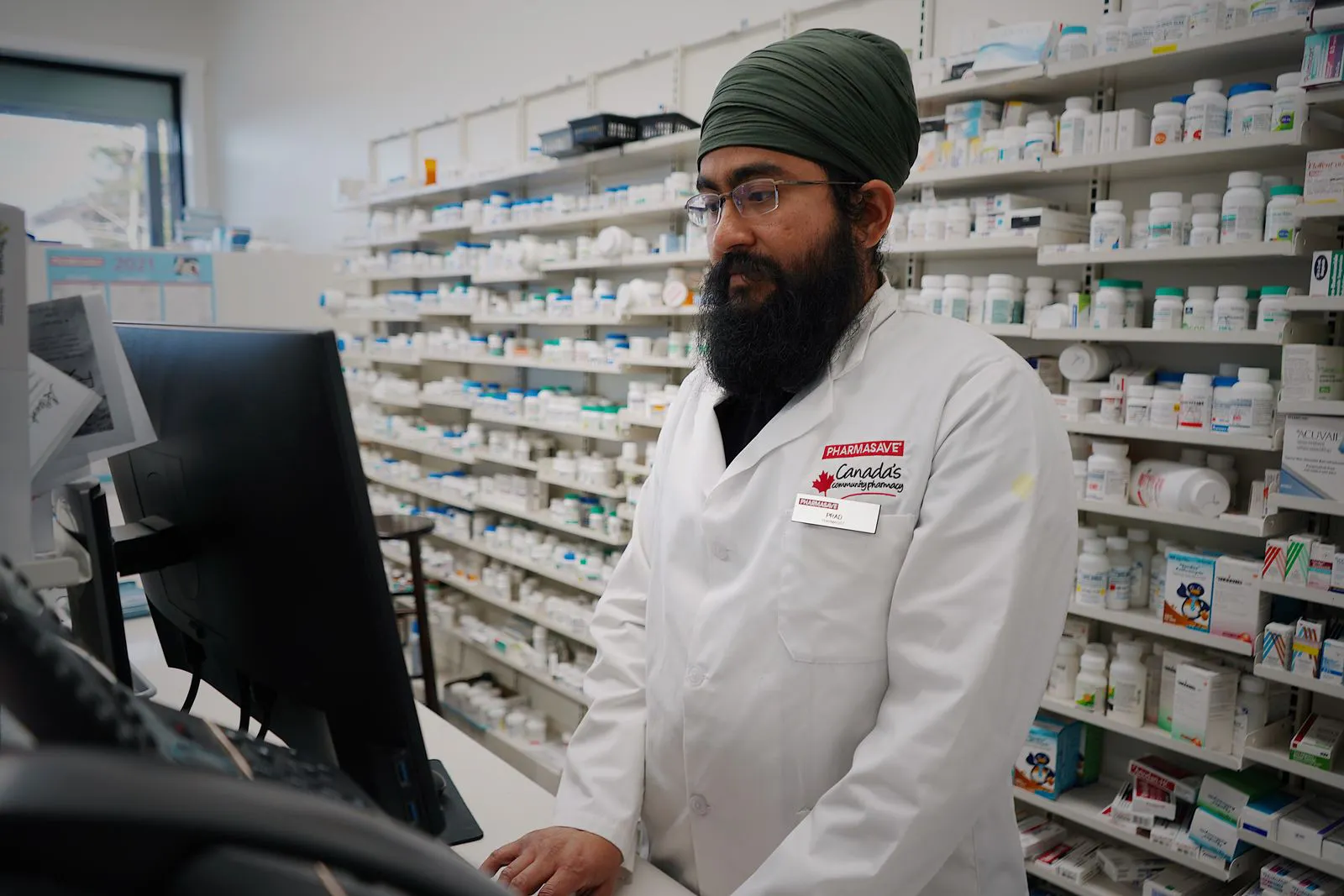 Pharmacist working at a computer, reviewing patient records in a pharmacy