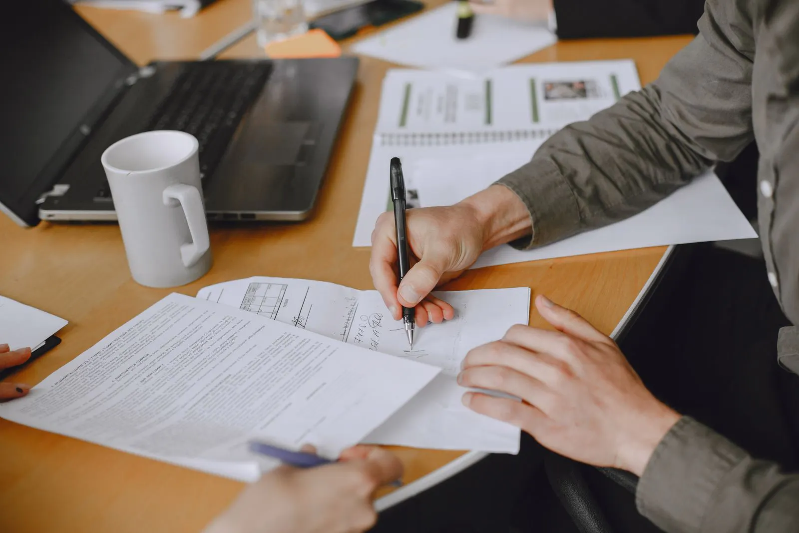 Two people reviewing and signing a document at a meeting table with a laptop nearby