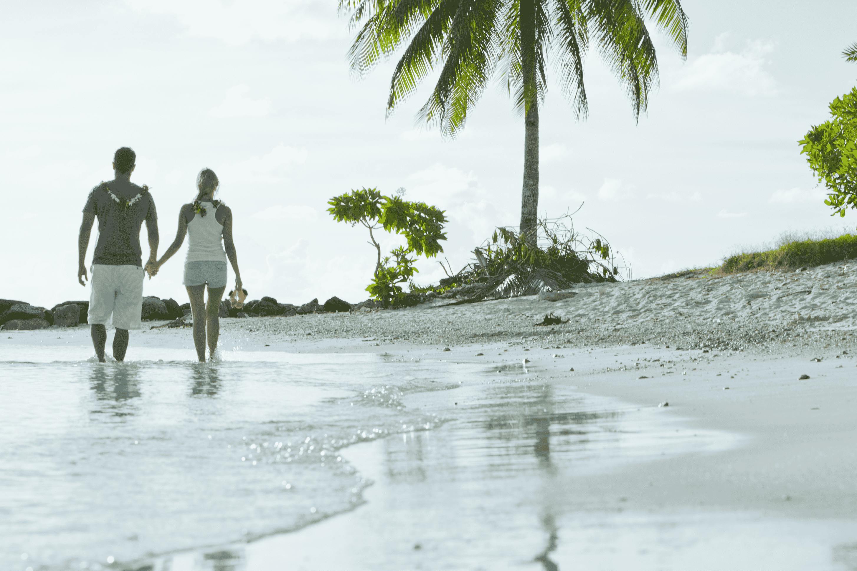 Promenade romantique sur une plage isolée à Huahine, avec un couple se promenant main dans la main le long du rivage, entouré de palmiers luxuriants et de vues sereines sur l'océan.