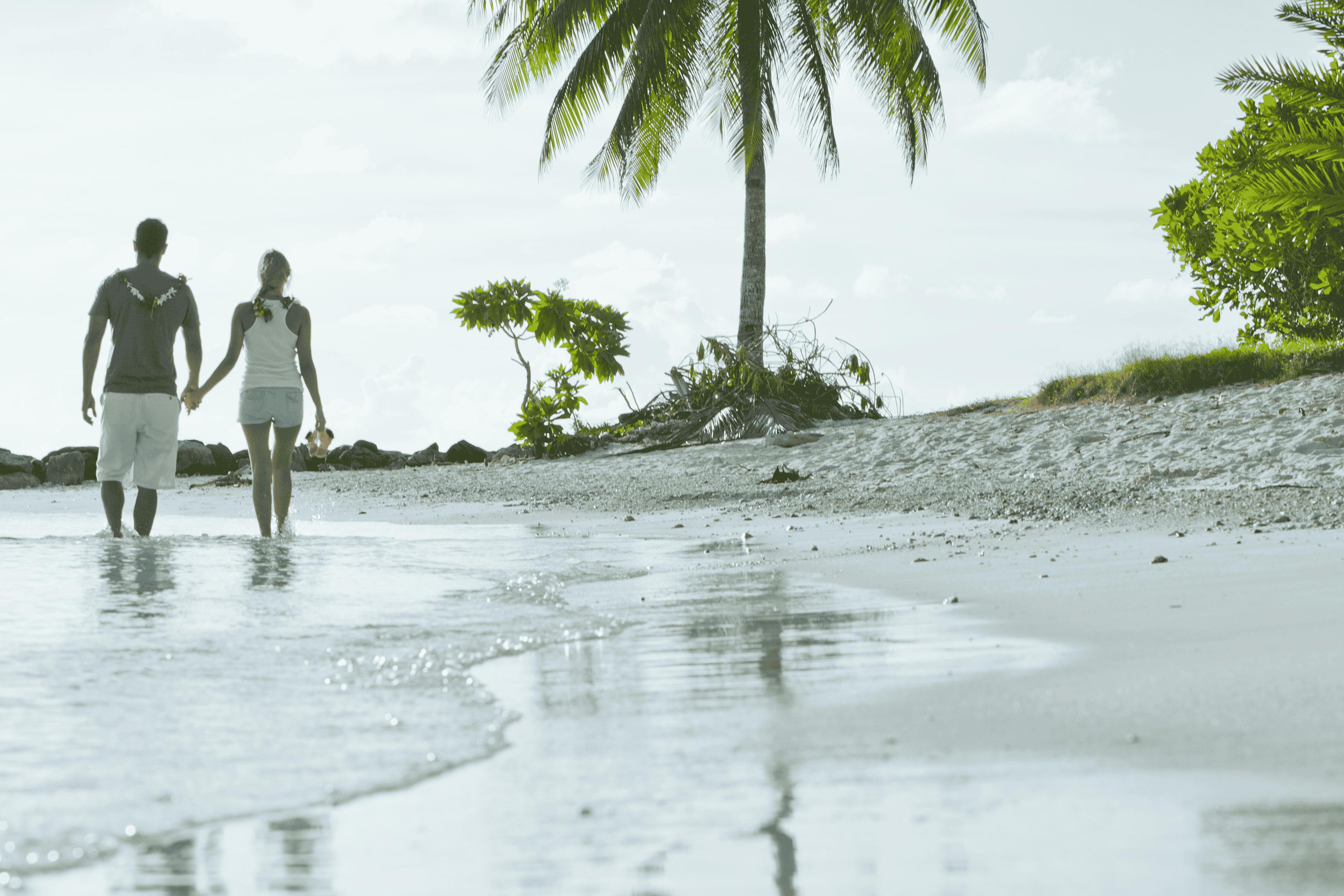 Romantic stroll on a secluded beach in Huahine, with a couple walking hand in hand along the shoreline, surrounded by lush palm trees and serene ocean views.