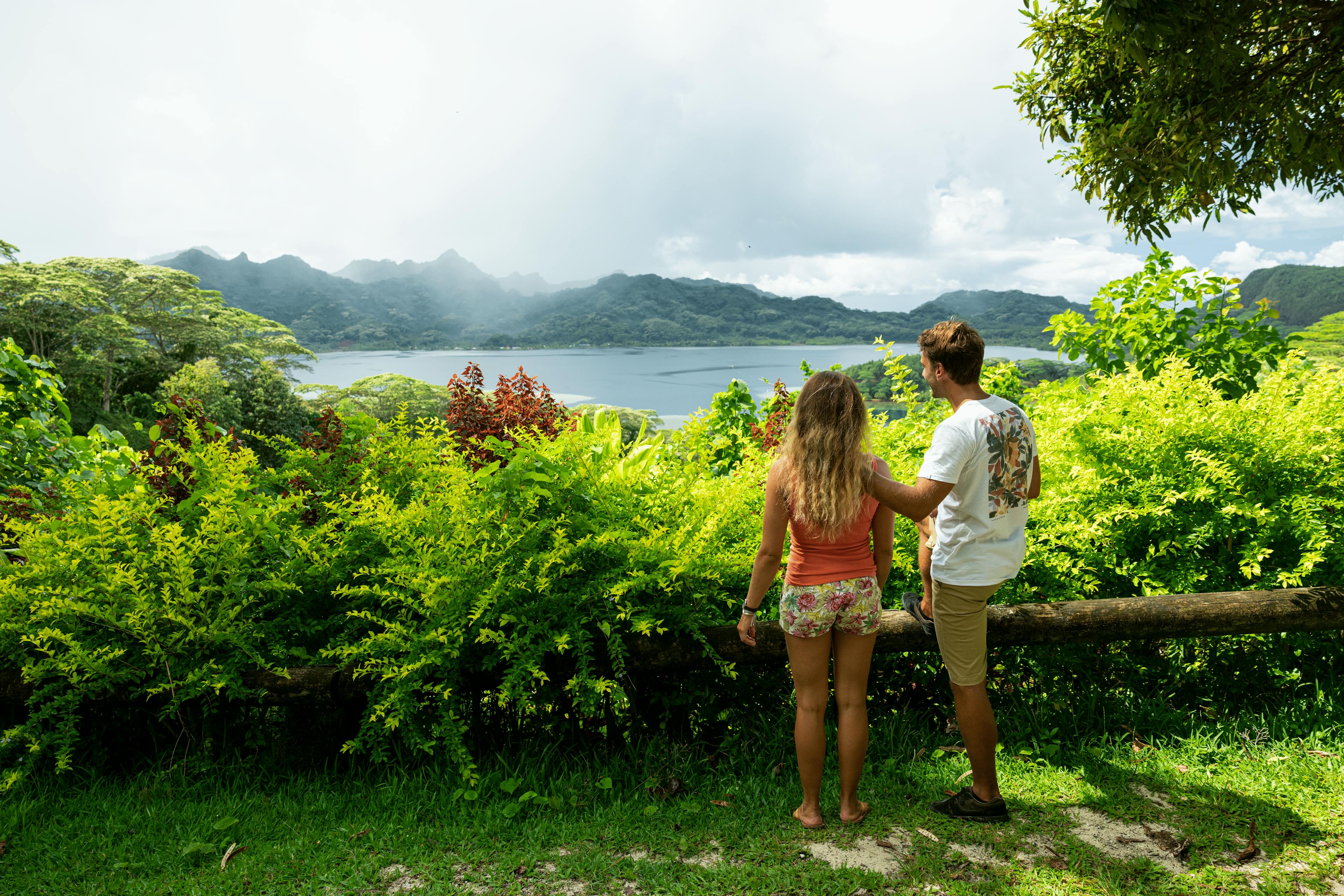 A couple standing on a viewpoint in Huahine, overlooking a lush green valley and tranquil waters, embodying a peaceful retreat in nature.