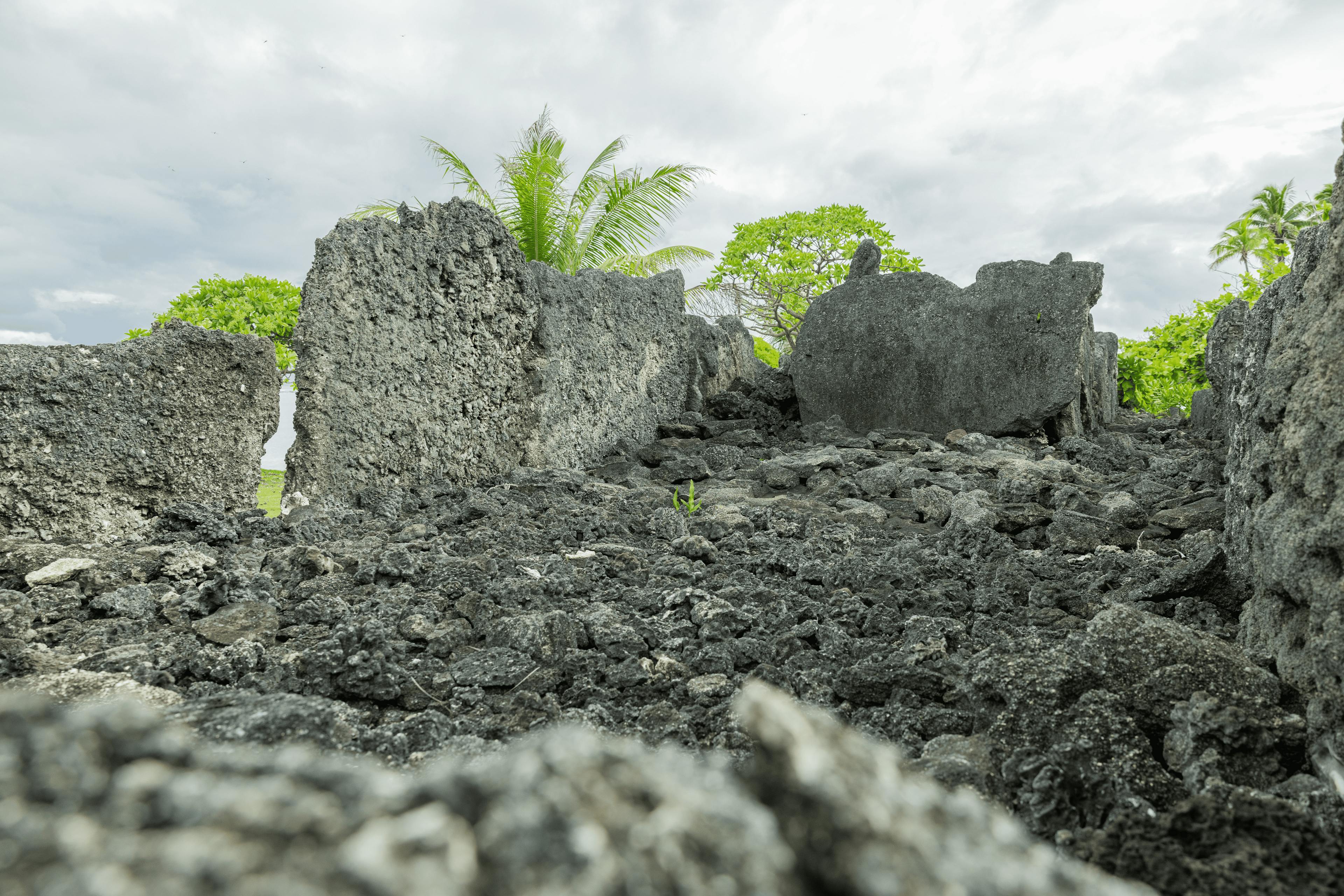 Rugged volcanic rock formations at a coastal site in Huahine, showcasing the natural geological history amid green tropical growth and a coastal backdrop.