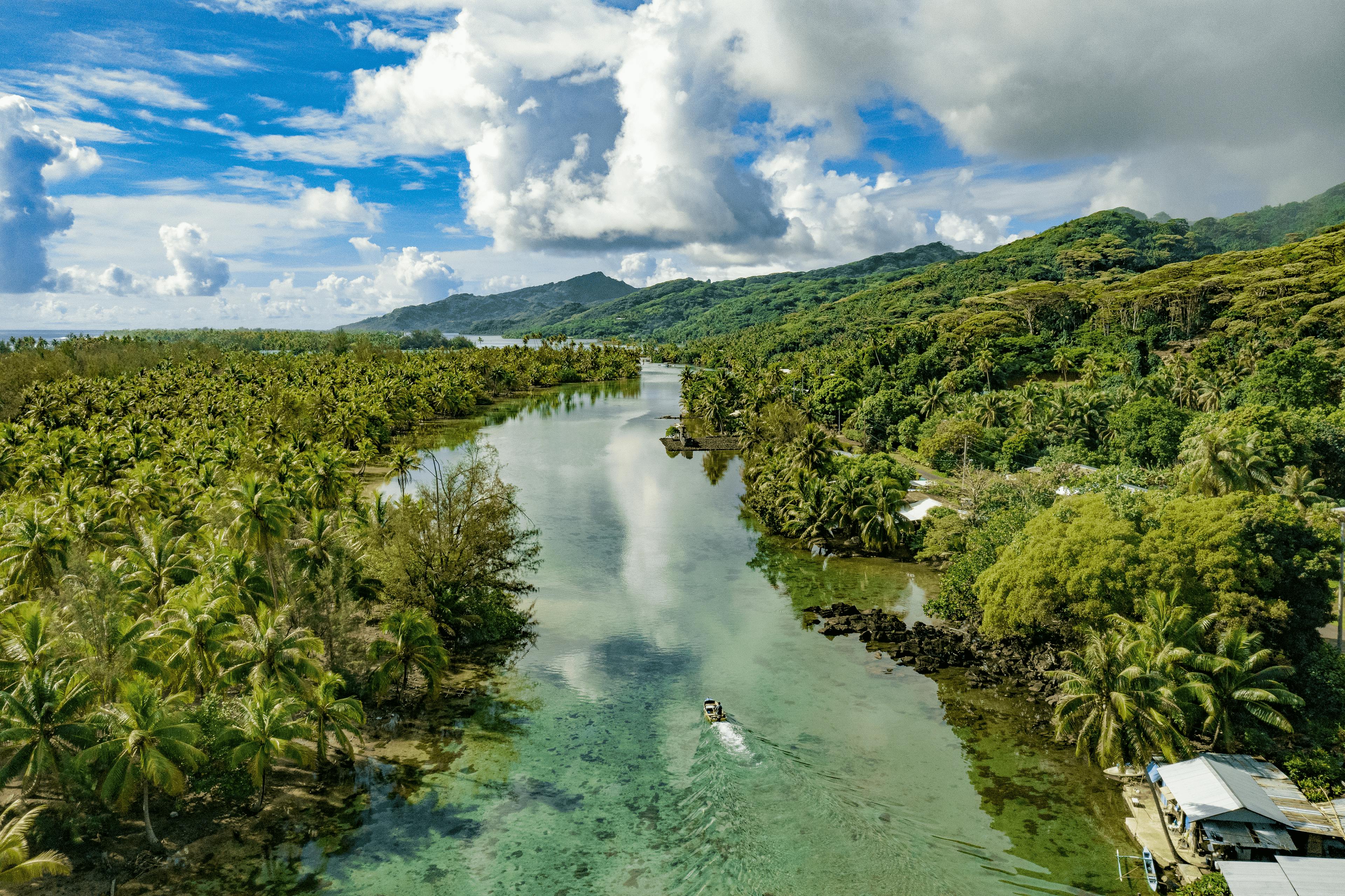 Aerial view of a vibrant lagoon in Huahine, showcasing the rich tapestry of tropical flora and serene waters, with a small boat cruising the channel.