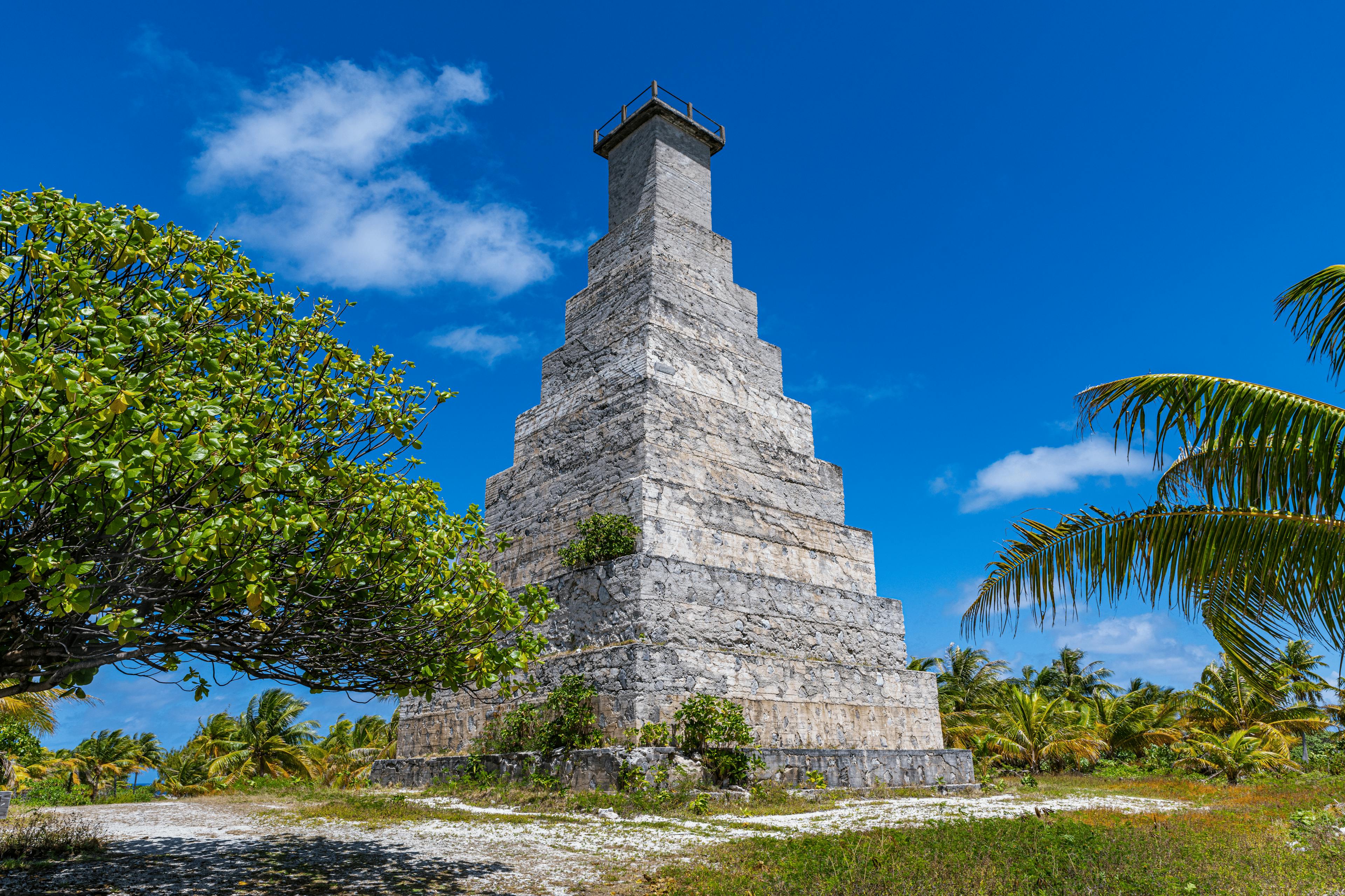 Un imposant monument en pierre de forme pyramidale se dresse sous un ciel bleu éclatant sur l'île de Fakarava. Entouré de palmiers et de végétation tropicale, il contraste avec le paysage sauvage et préservé de l’atoll.