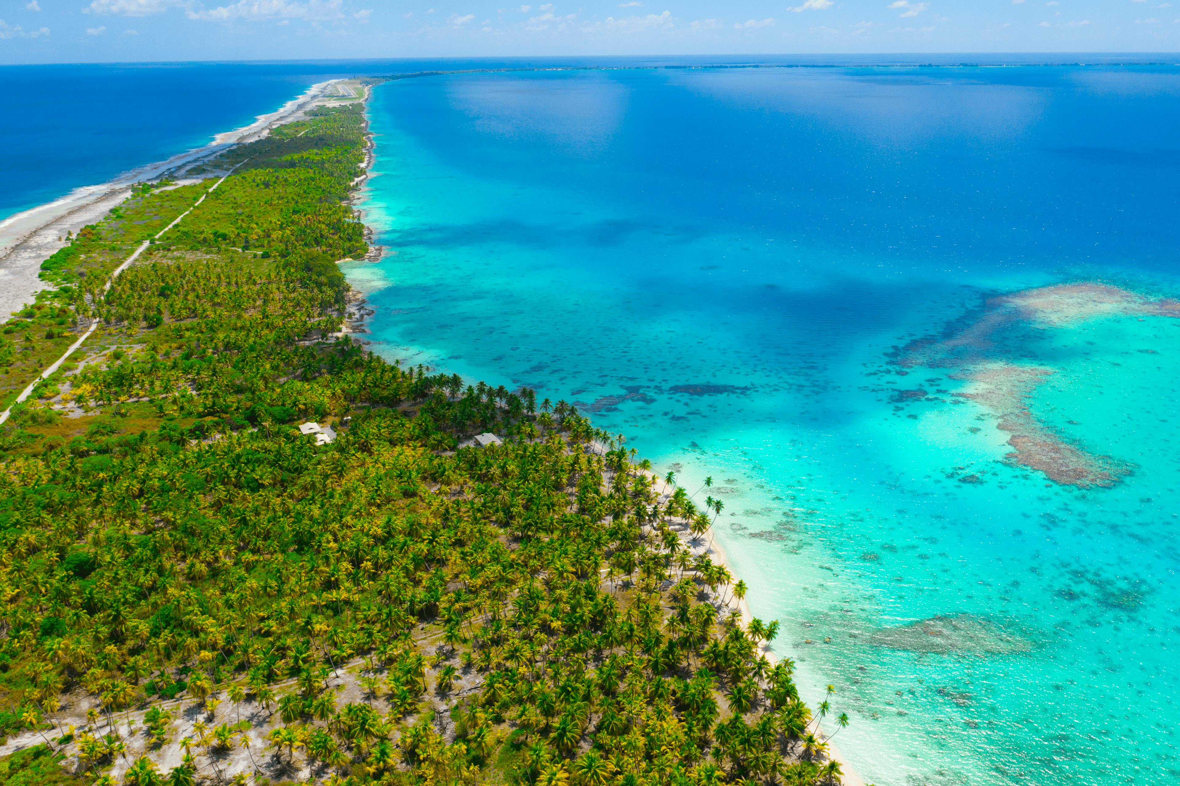 Vue aérienne de la longue bande de terre de Fakarava, séparant le lagon aux eaux cristallines de l’océan. Le paysage est ponctué de cocotiers et de petites habitations, offrant une perspective saisissante sur la nature préservée de l’atoll.