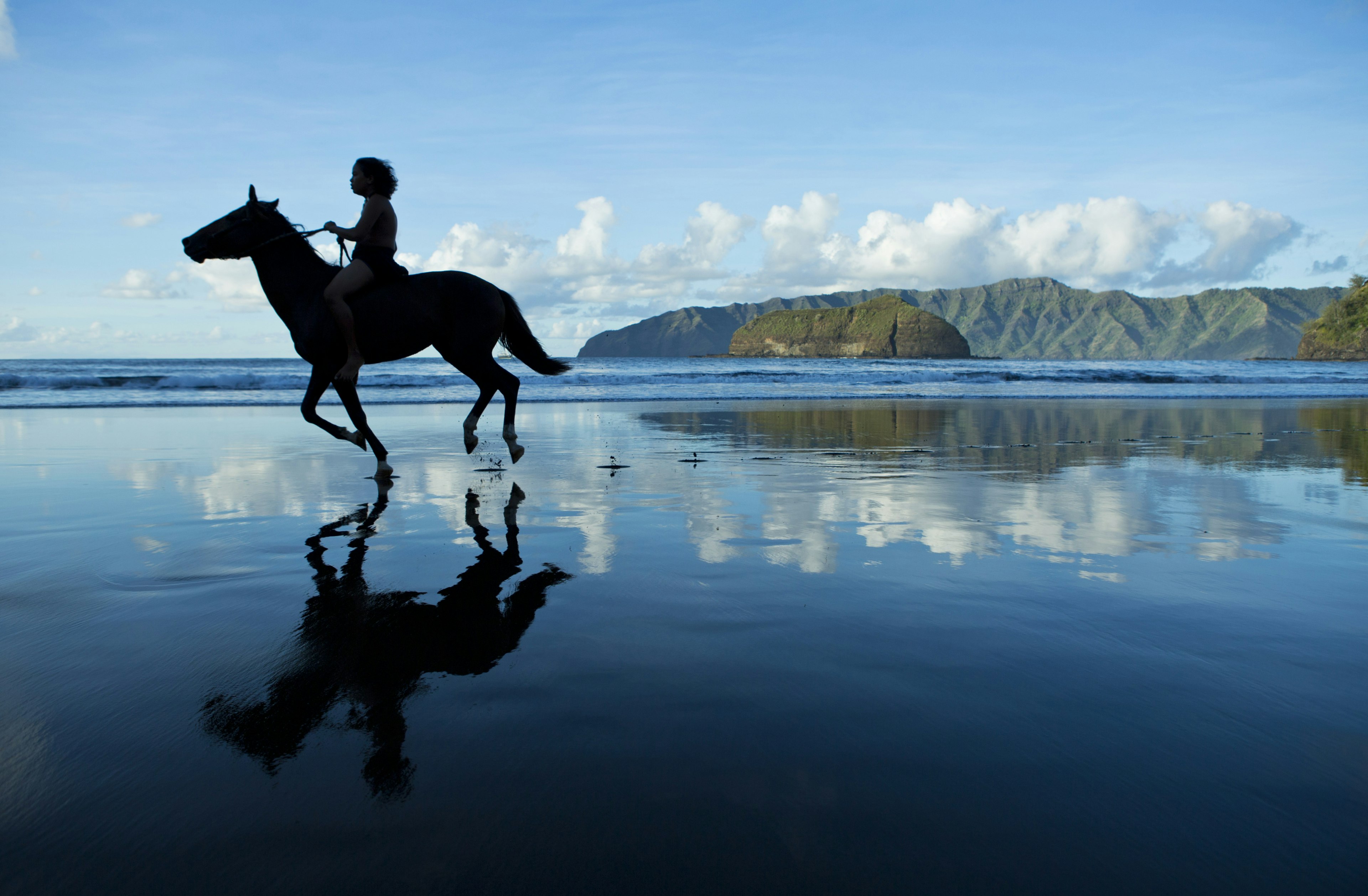 Polynesian horseman gallops on the sand in Hiva Oa