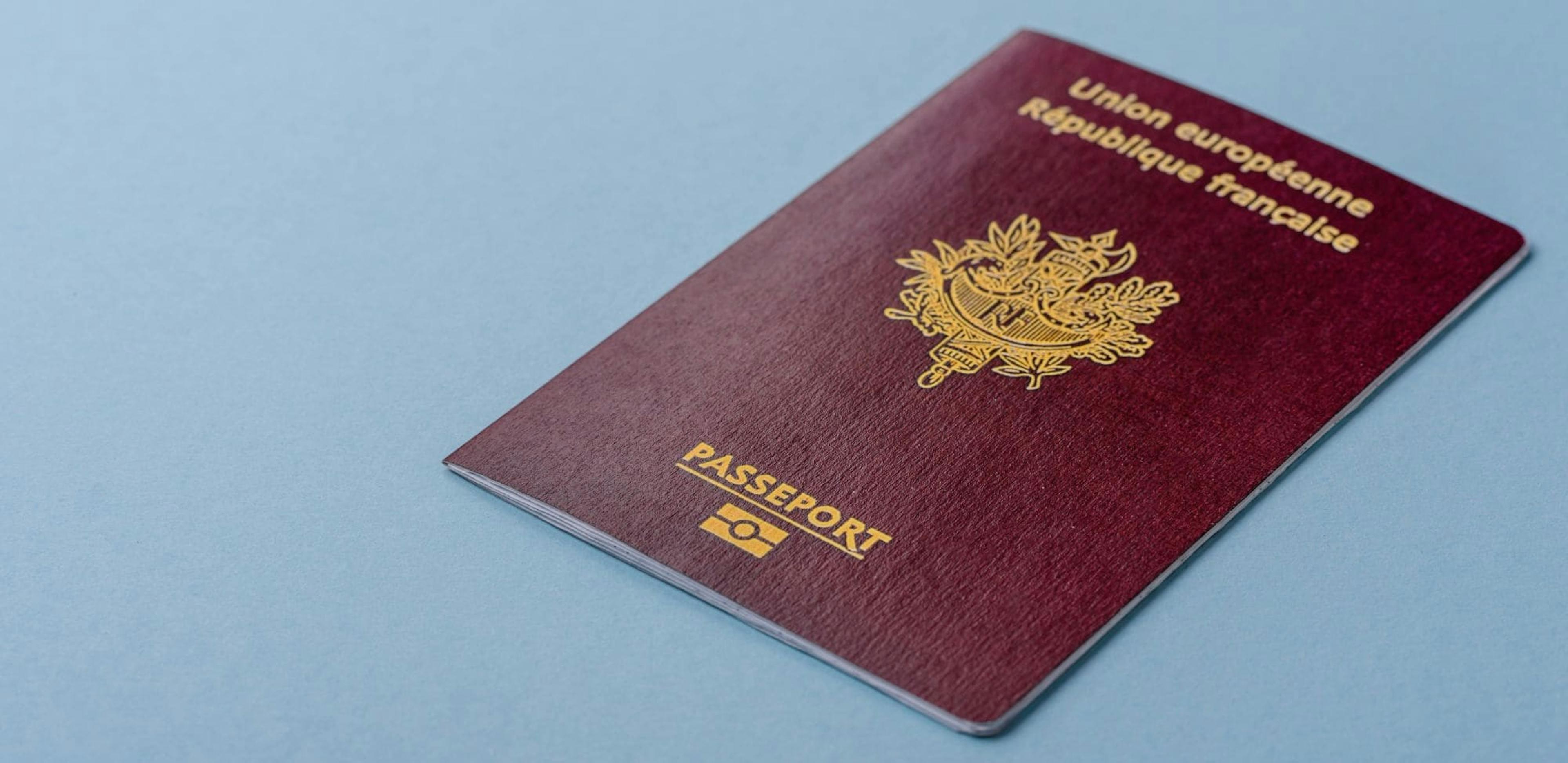 A French Republic passport, burgundy in color, placed on a blue background. The passport features the inscriptions 'European Union' and 'French Republic' in gold letters, along with the word 'Passeport' and a biometric symbol at the bottom.