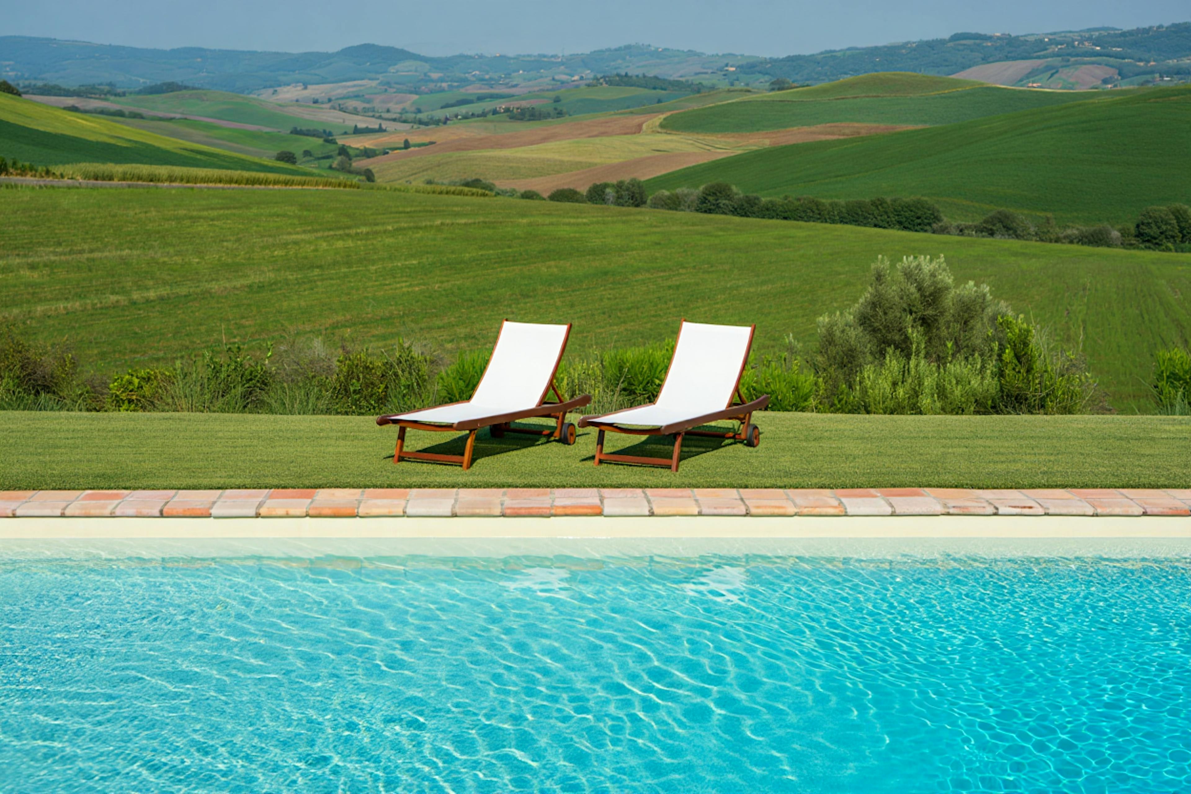 picture of two lounge chairs by the pool with country side landscape