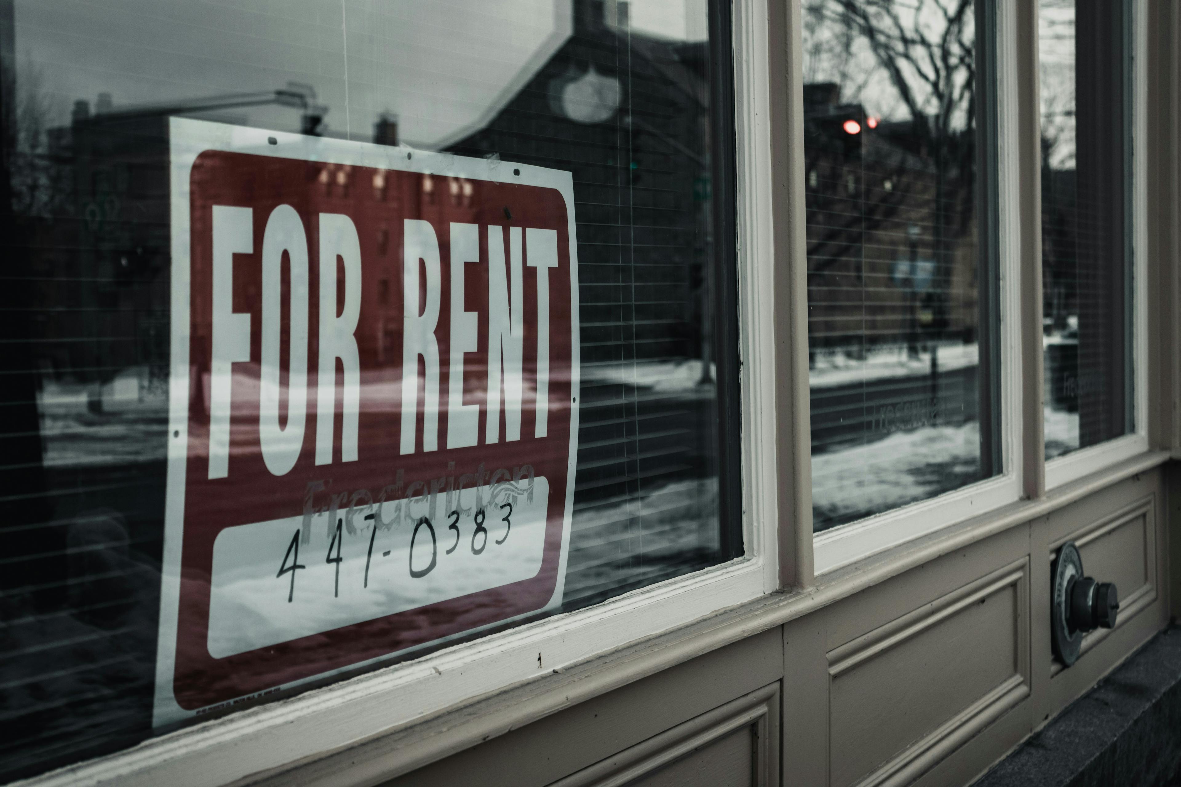 A picture of a 'For Rent' sign in a house window