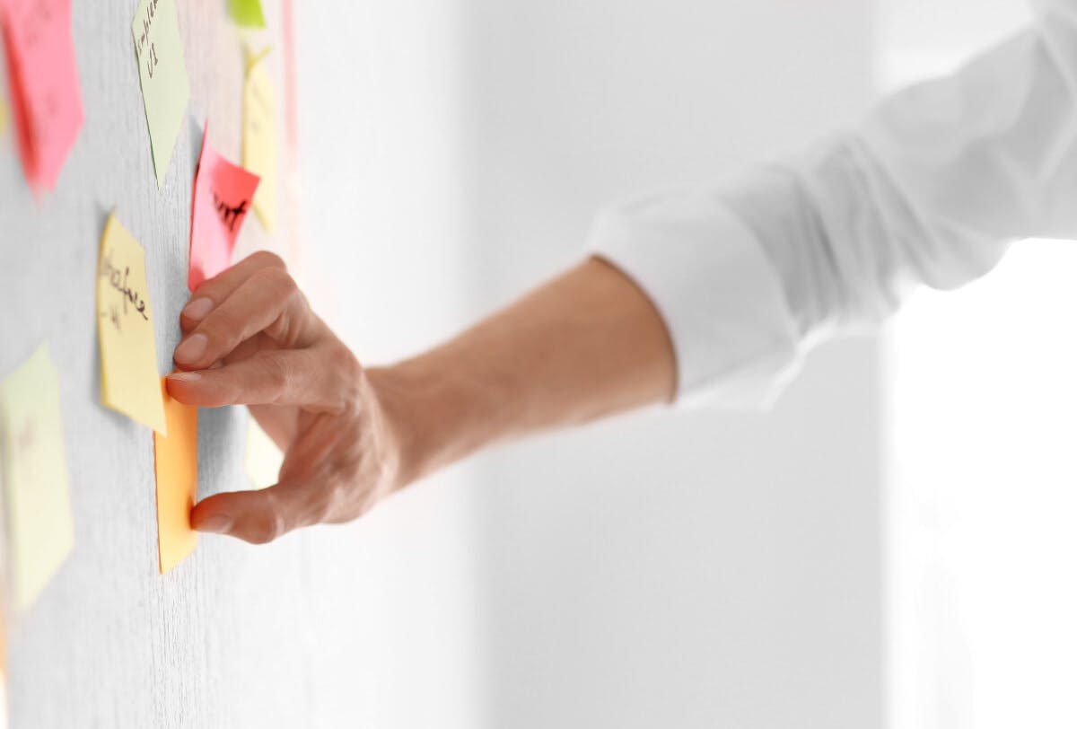 A hand on an orange sticky note as part of a project management system