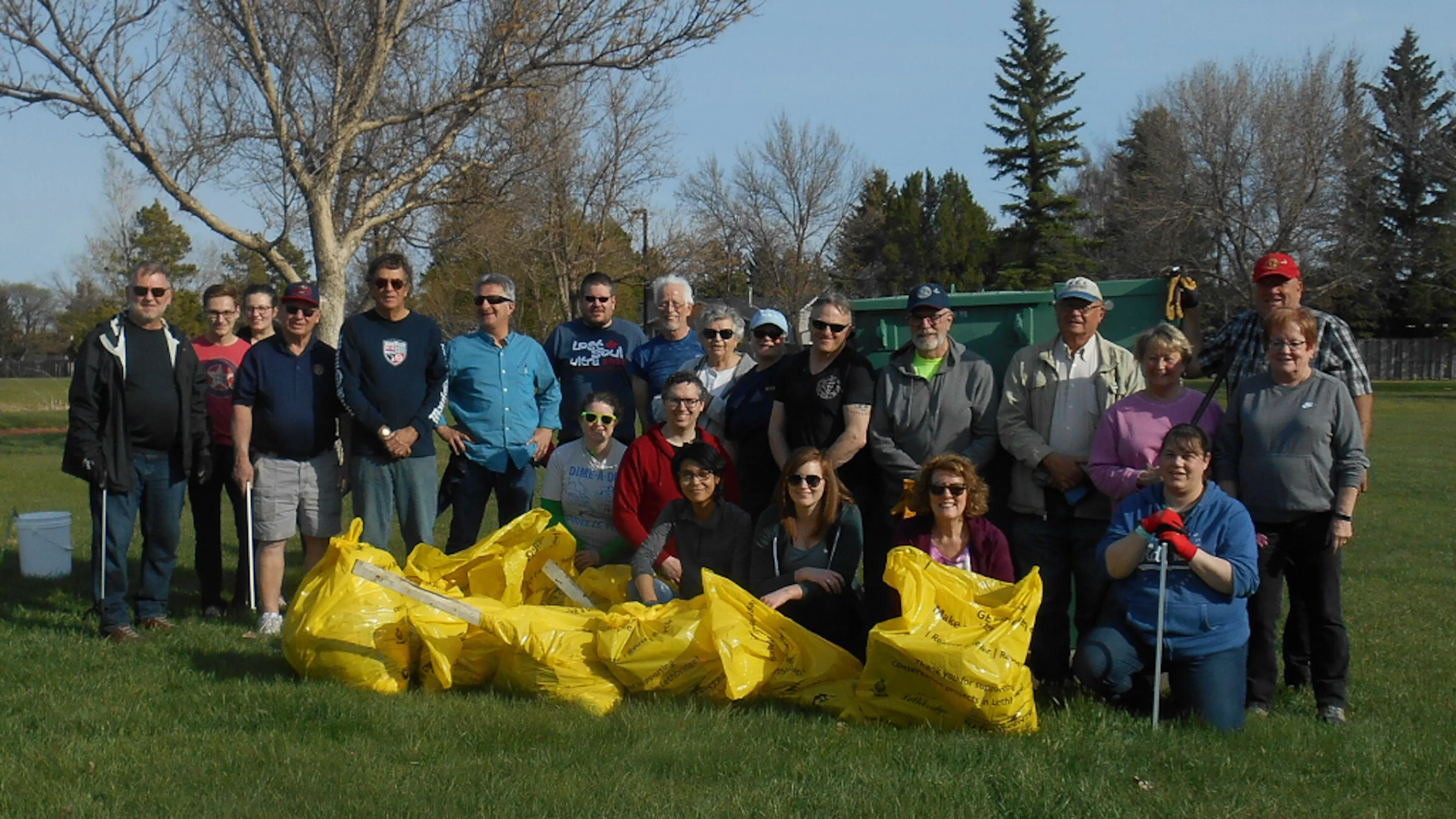 Large group of people together in front of yellow garbage bags.