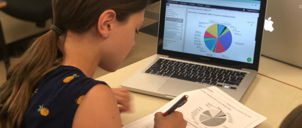 Child sitting at a desk looking at a circle graph on a piece of paper and laptop