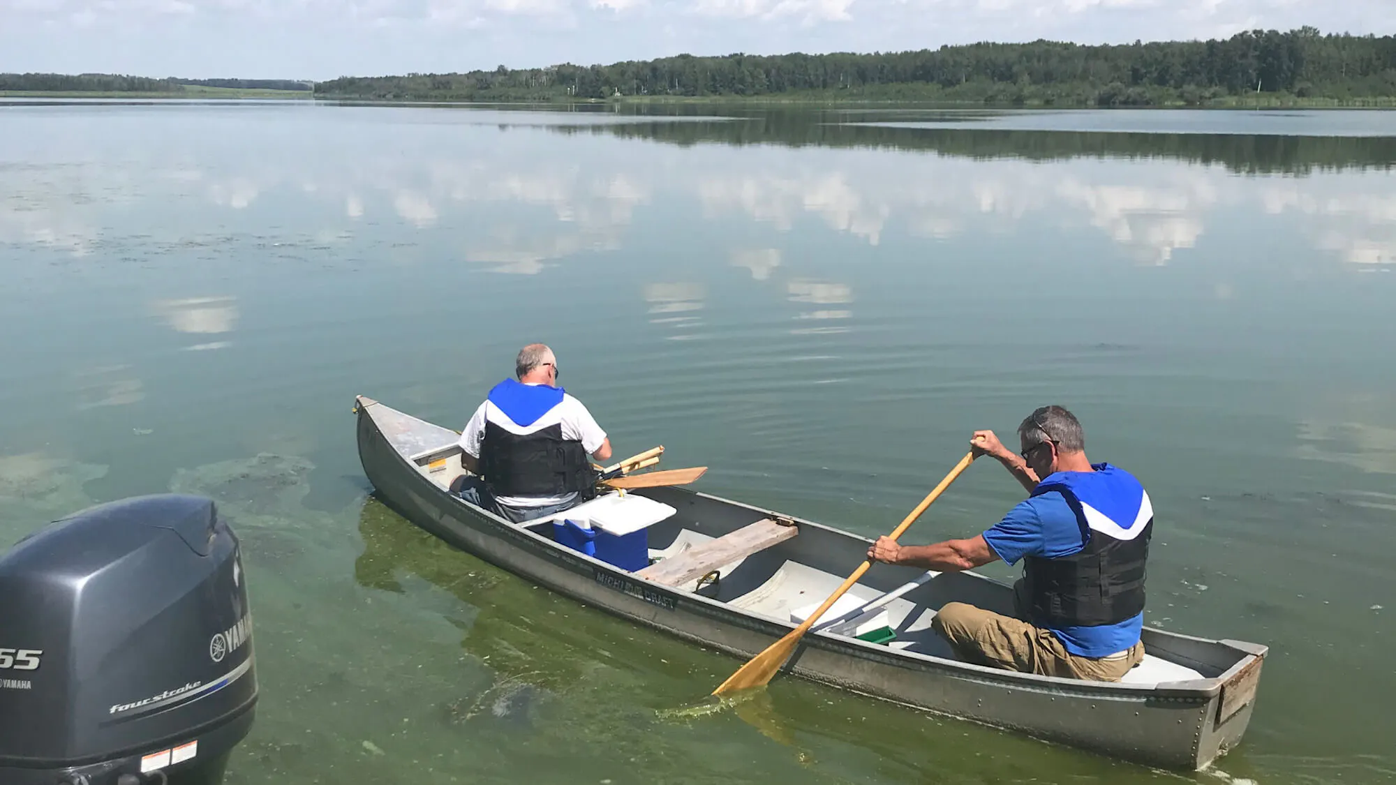Two men in blue outfits sit in a canoe in a lake.