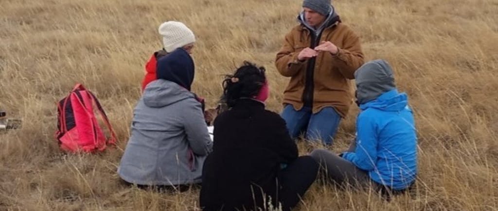 Group of people sitting in the grass learning from a teacher