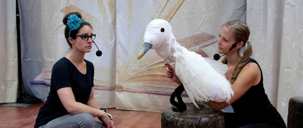 Two people on a stage and one is holding a bird puppet