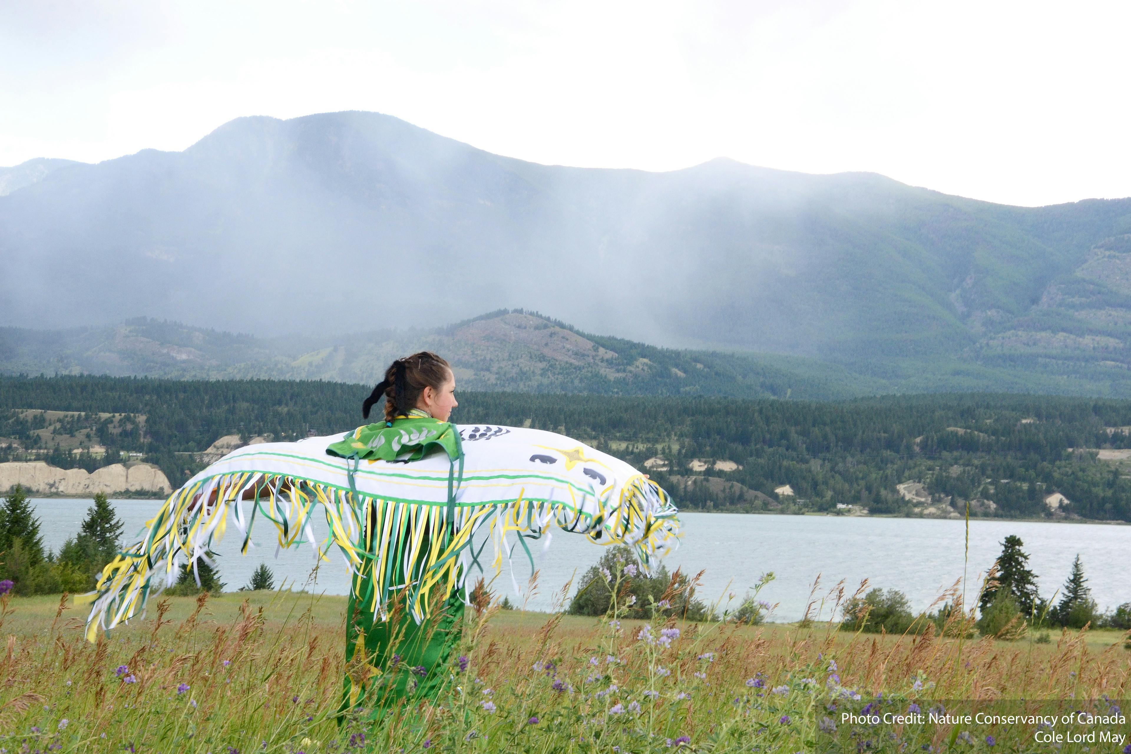 Indigenous woman looking at a lake and opening her arms as if flying