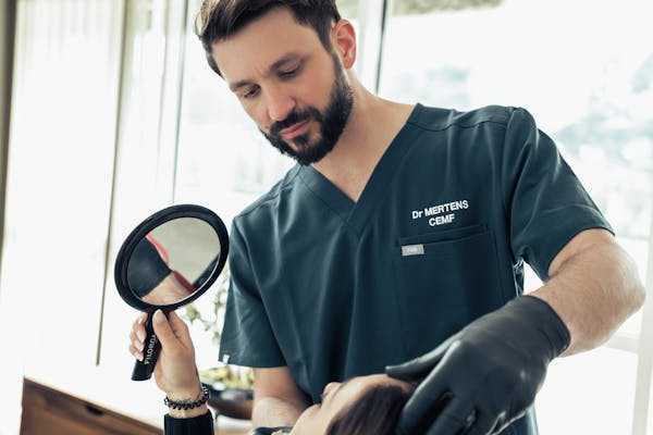 Expert réalisant des injections d'acide hyaluronique sur une patiente qui regarde ensuite le résultat dans le miroir.