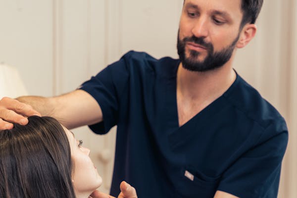 Chirurgien qui analyse le visage d'une jeune femme en vue de réaliser une rhinoplastie.